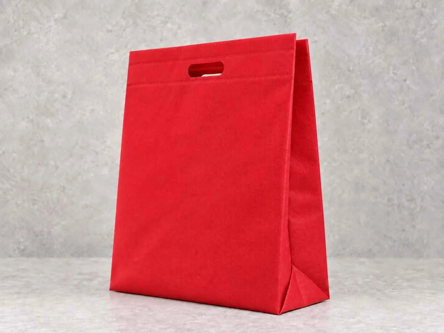 A red paper gift bag with a handle cutout on a gray textured background.