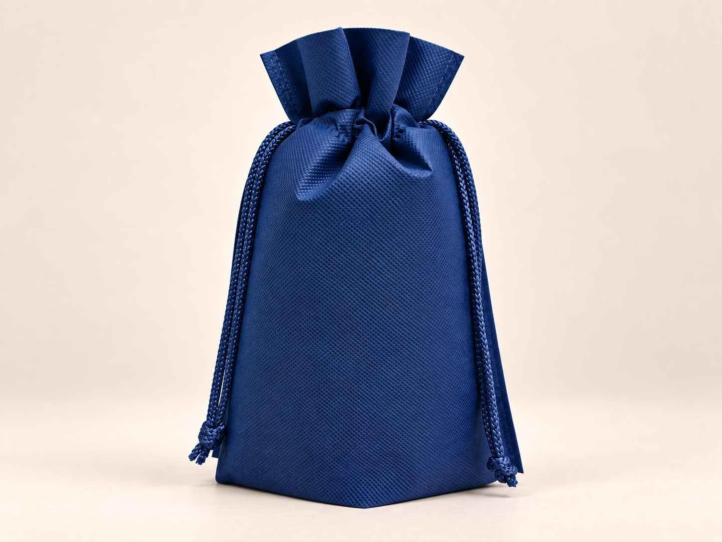 Bolsa en cambrel caramelo fuelle abajo reutilizable color azul oscuro con cordones sobre un fondo neutro.