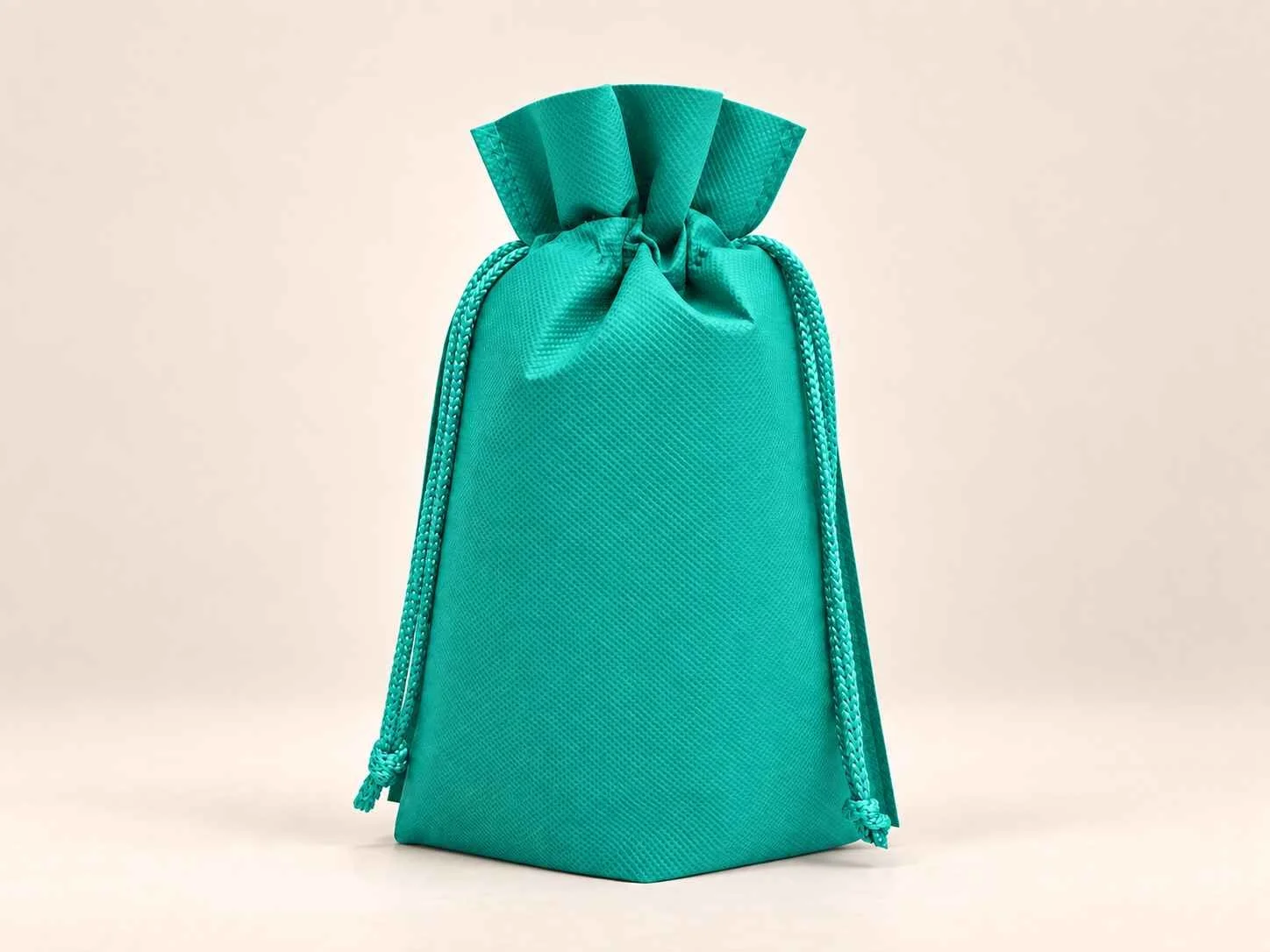 Bolsa en cambrel caramelo fuelle abajo reutilizable color verde jade con cordones sobre un fondo neutro.