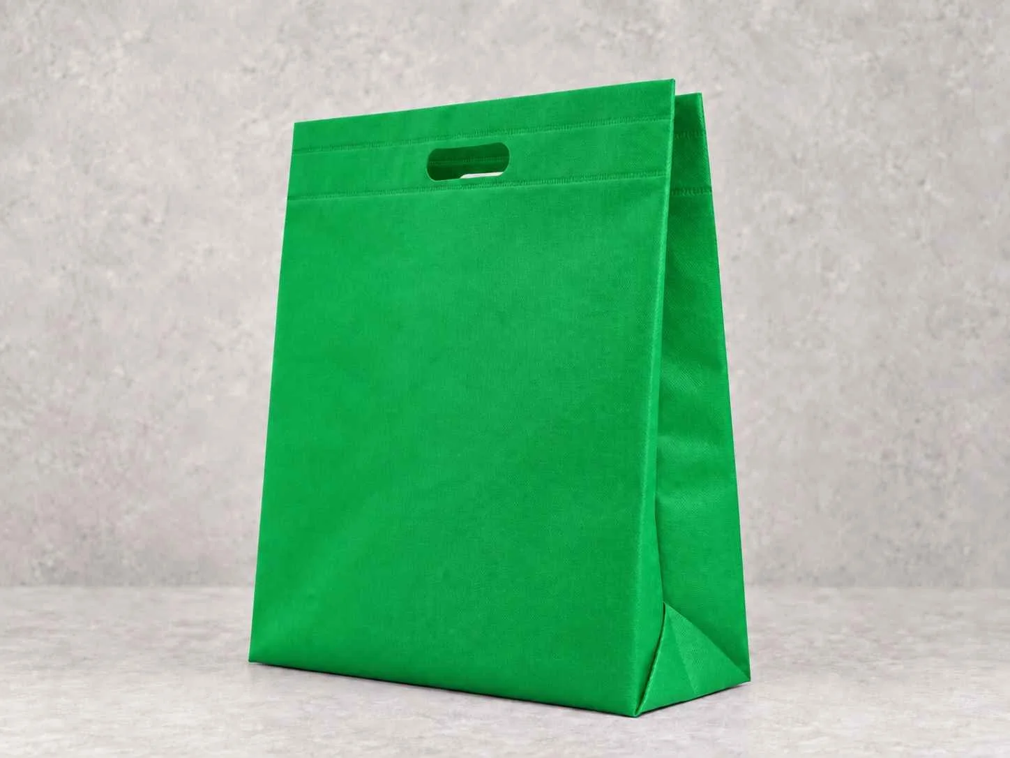 Green cambrel bag with cut-out handle on a light textured background.