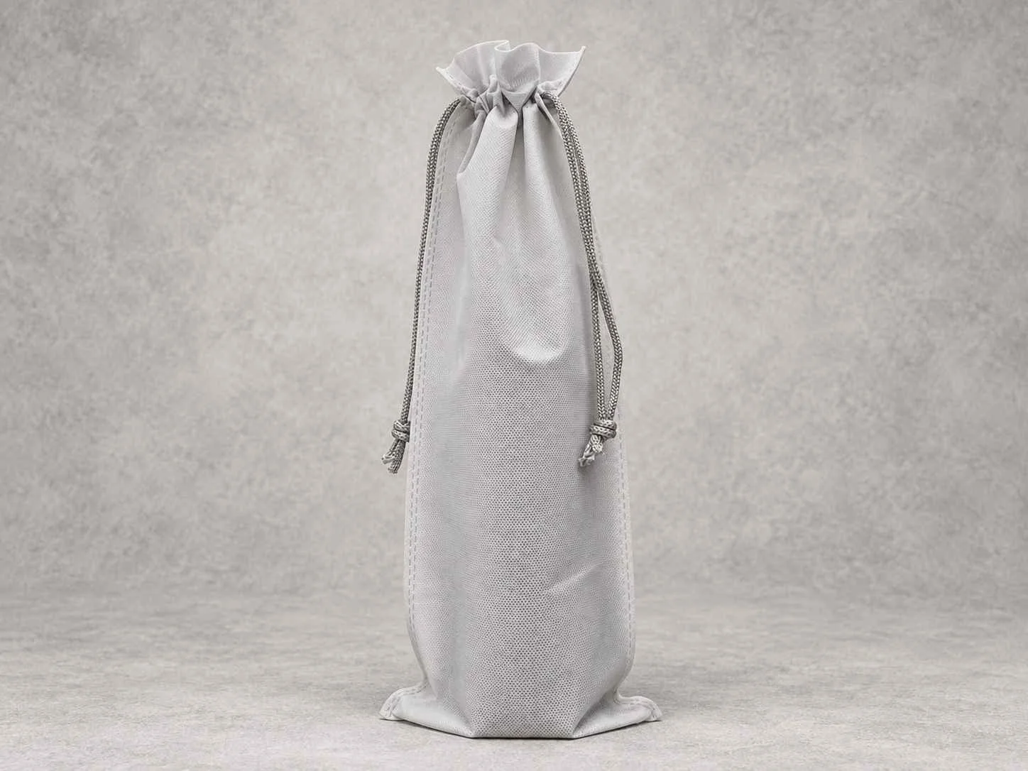 Gray fabric drawstring gift bag with knotted cords on a light textured background.