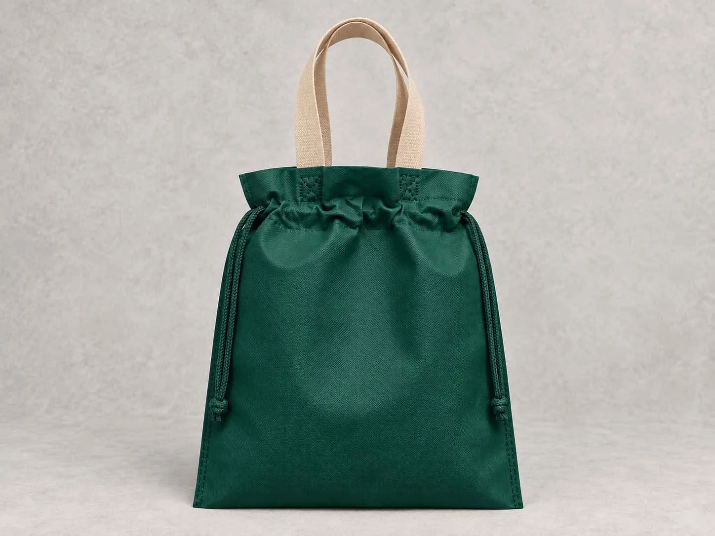 
Una bolsa reutilizable plana fusión verde oscuro con manija beige de cambrel de pie vertical sobre una superficie neutra contra un fondo neutro.