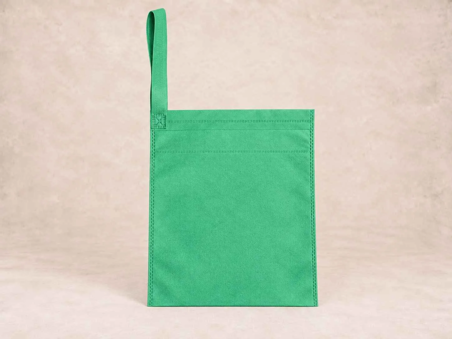 Green reusable tote bag with a single handle against a light beige background.