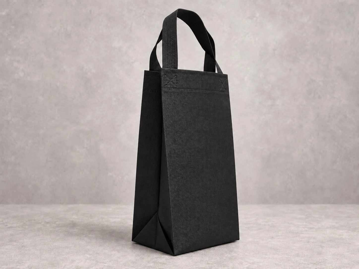 A black reusable shopping tote bag standing upright on a gray surface with a matching gray background.