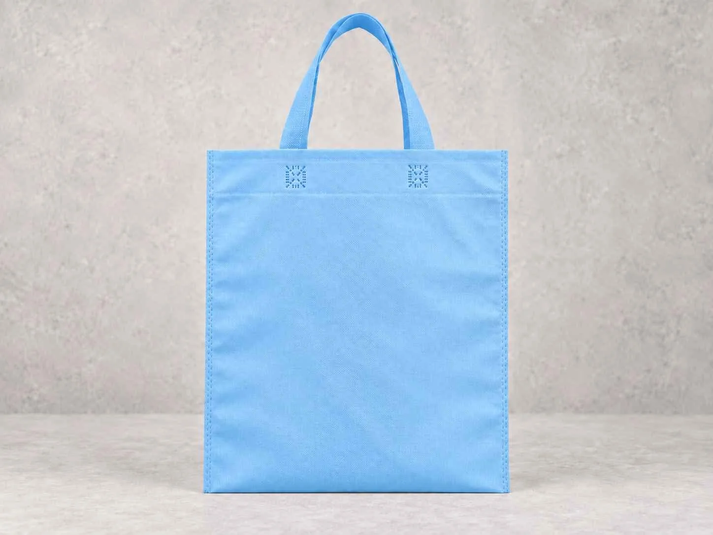 Light blue reusable shopping bag with handles, standing against a light gray textured background.