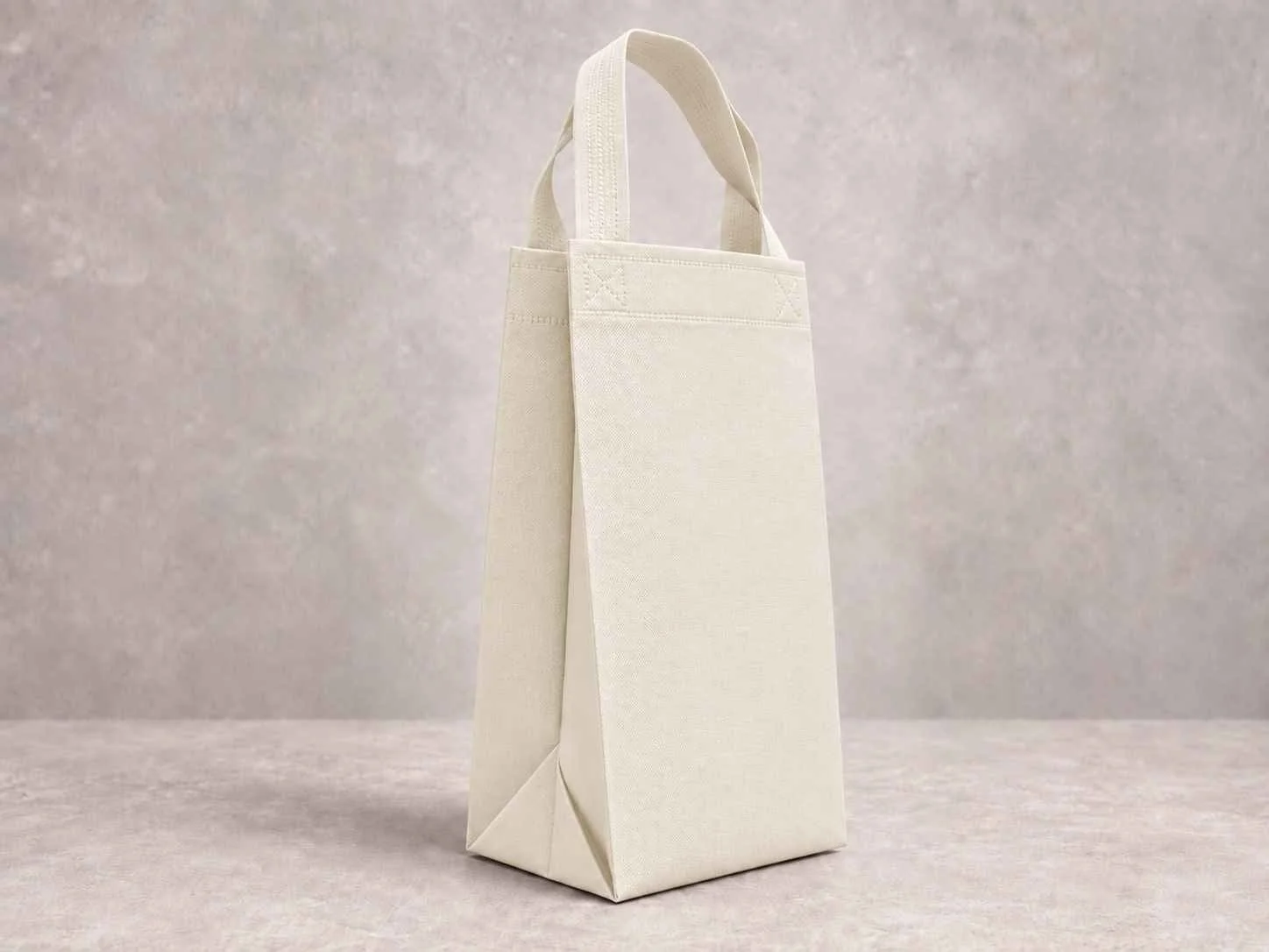 A plain, off-white, reusable tote bag standing upright on a grey textured surface with a matching grey textured background.