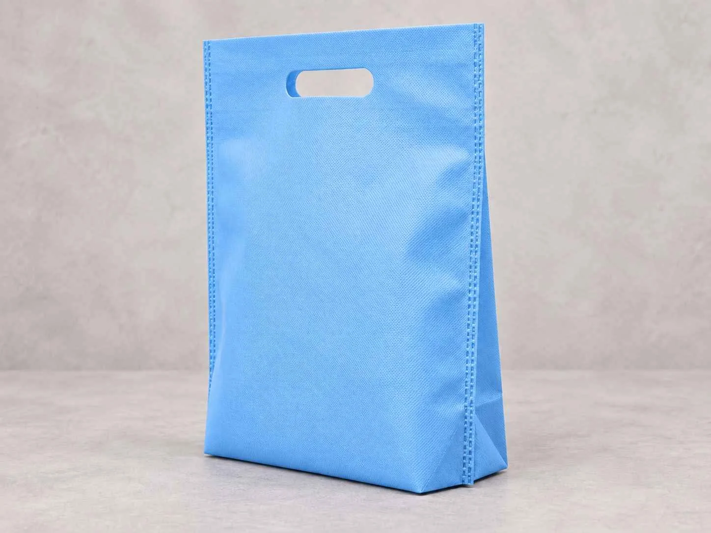 A blue bolsa reusable de cambre plana con fuelle abajo standing upright on a neutral surface against a neutral background.