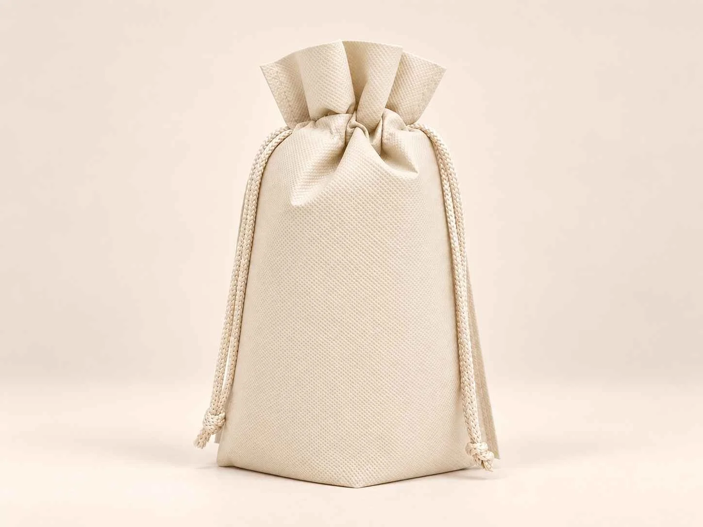 Bolsa en cambrel caramelo fuelle abajo reutilizable color marfil con cordones sobre un fondo neutro.