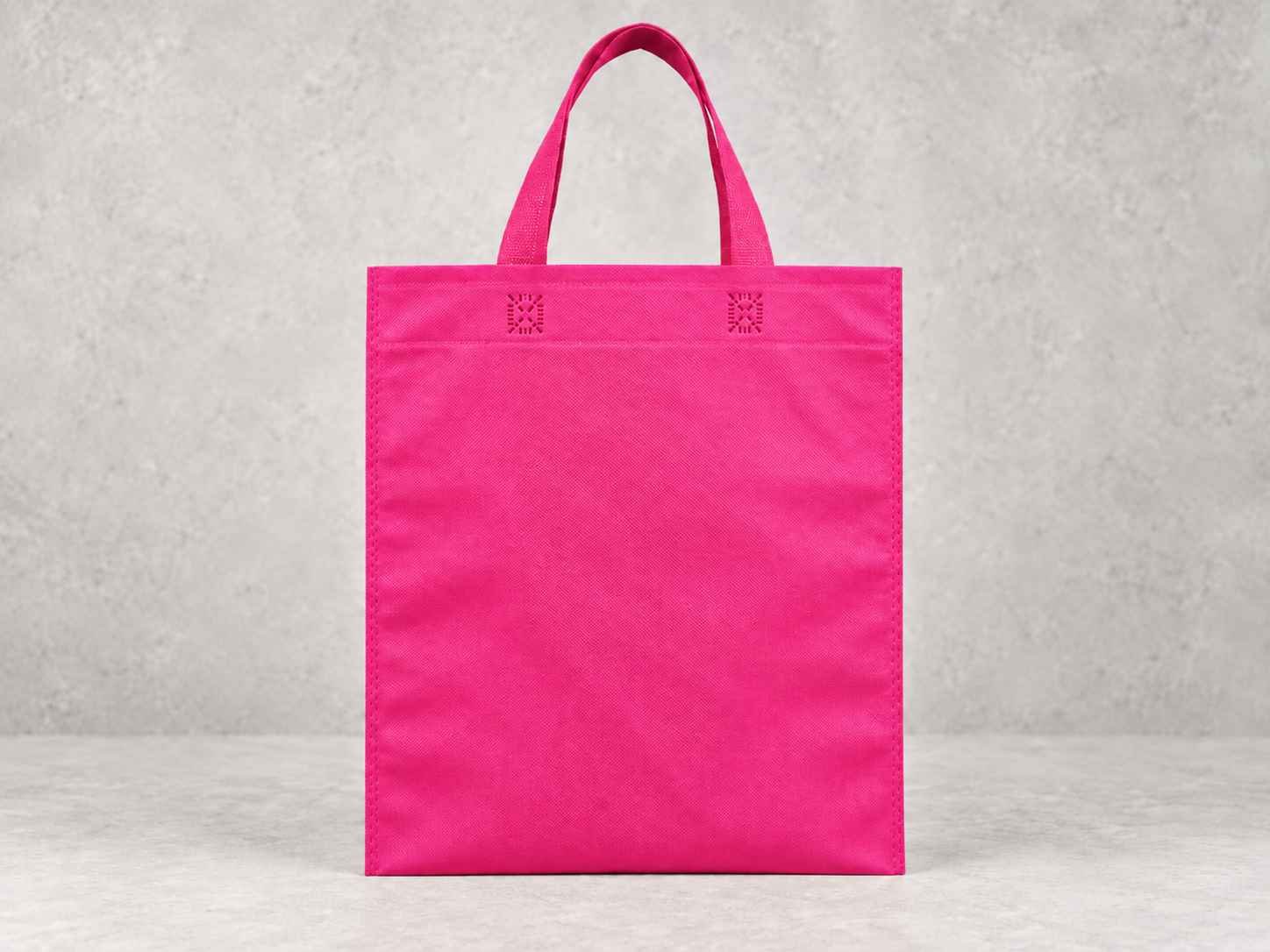 Pink reusable tote bag standing against a gray textured background.