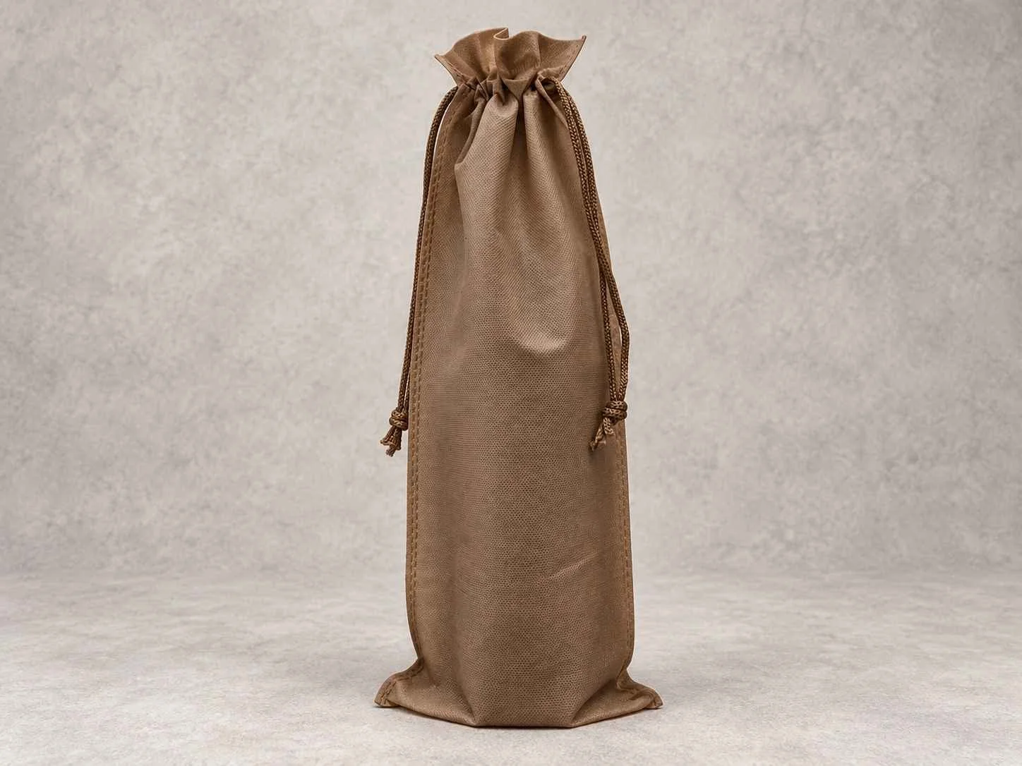 A tall, brown fabric bag with a drawstring closure, standing upright on a neutral background.
