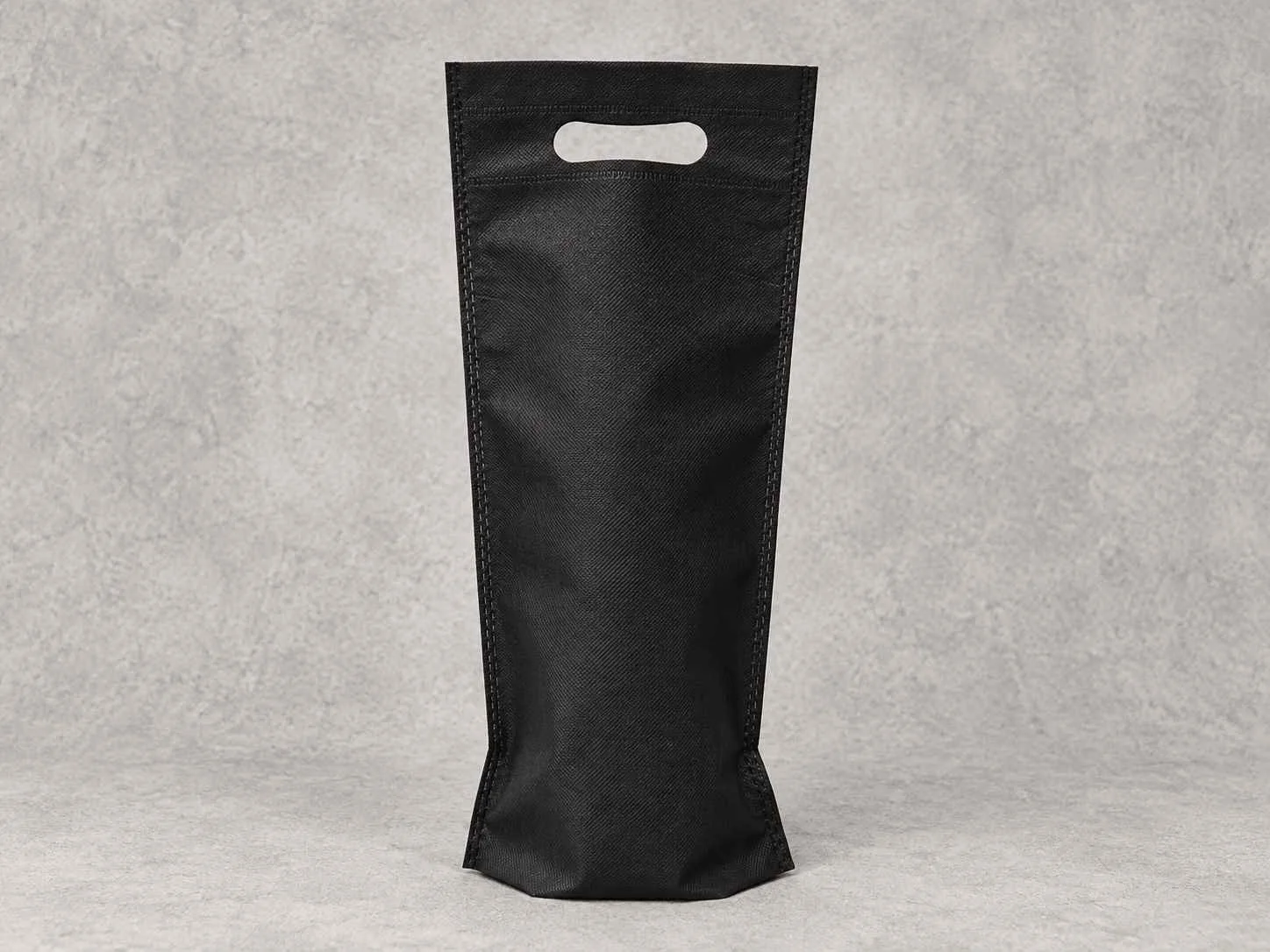 Black shopping tote bag with cutout handles standing upright on a light gray surface.