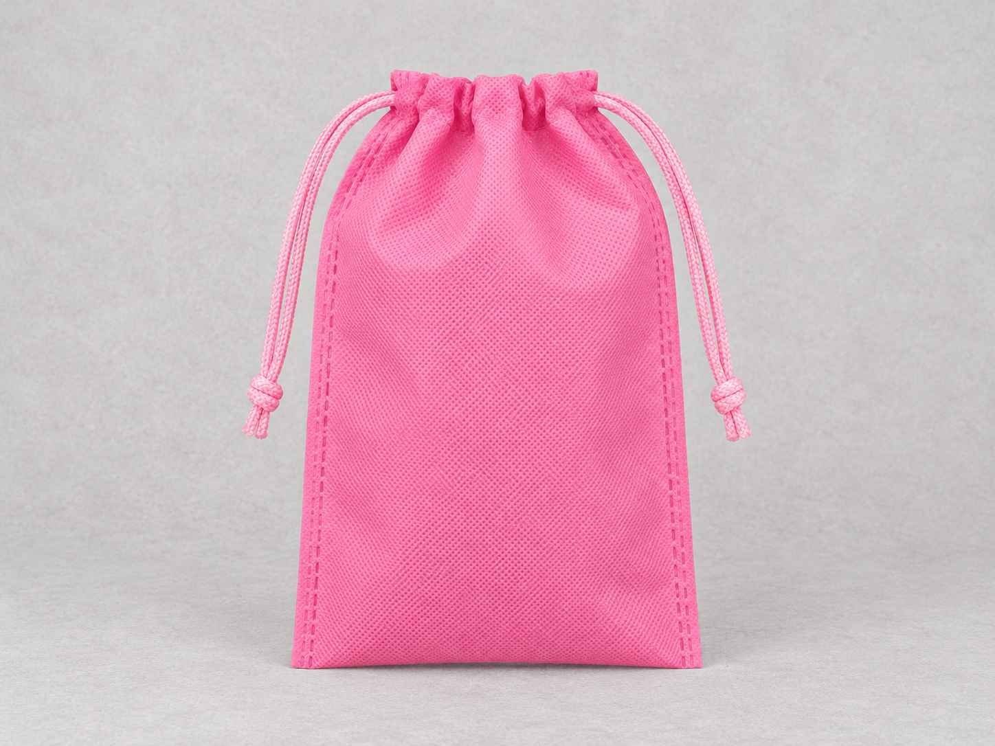 Pink drawstring pouch made of cambrel fabric on grey background.