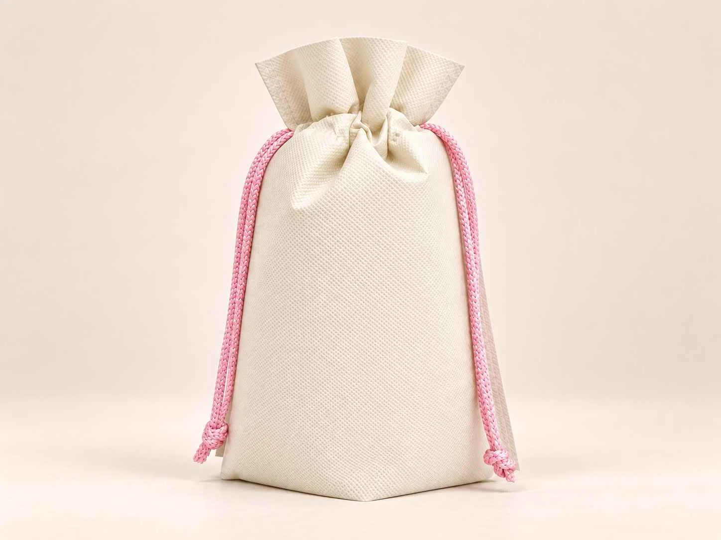 Bolsa en cambrel caramelo fuelle abajo reutilizable color marfil con cordones rosado sobre un fondo neutro.