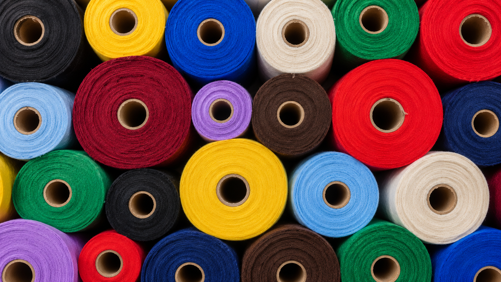 Multiples rollos de tela cambrel arranged closely together, featuring colors such as red, yellow, blue, green, black, white, purple, and brown.