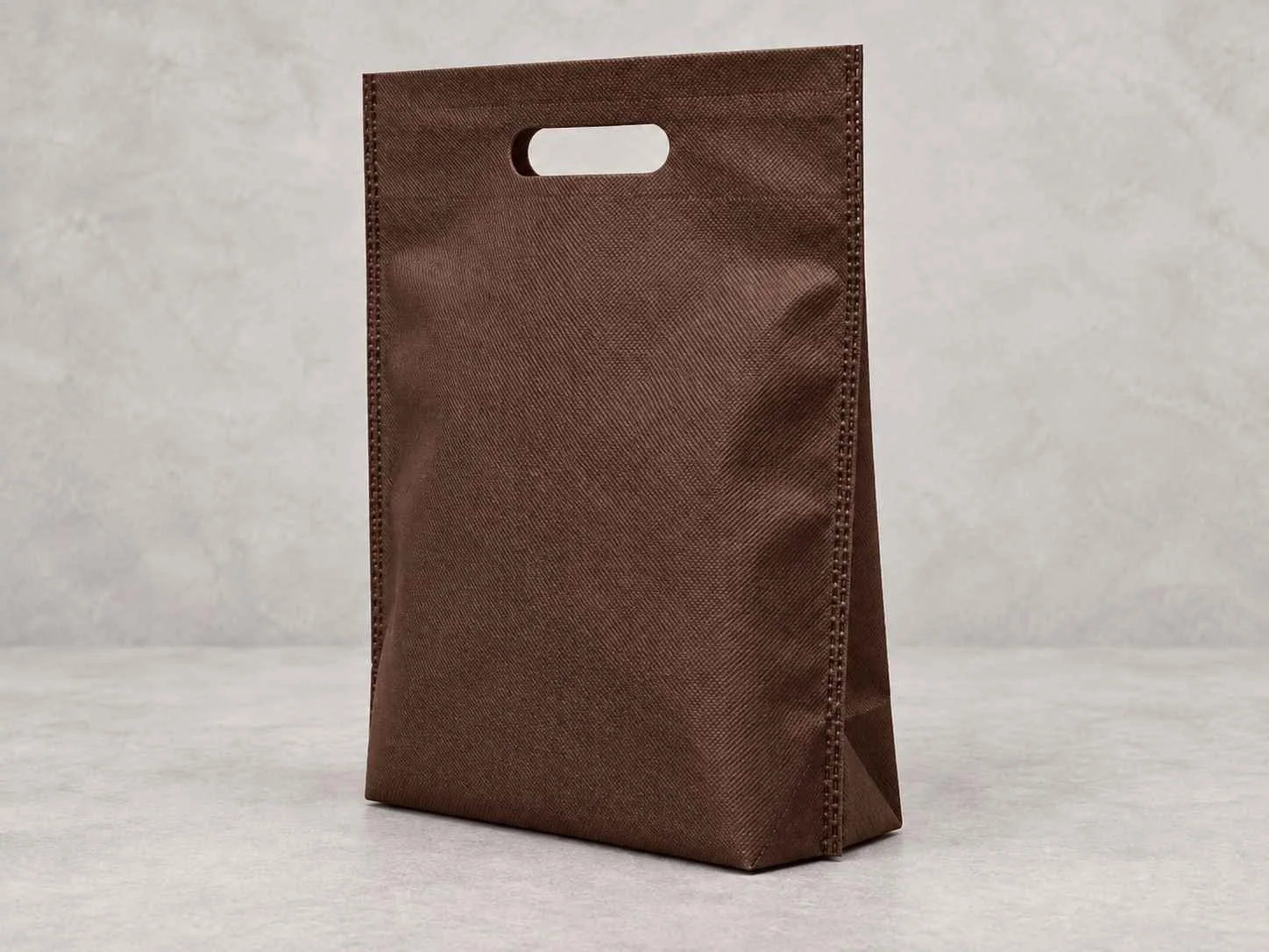 A brown bag de cambre plana troquel con fuelle abajo, standing upright on a flat surface against a neutral background.