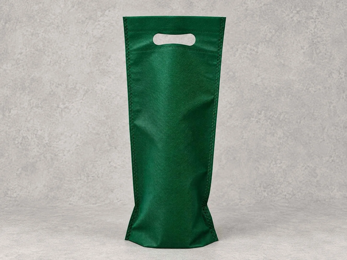 Green fabric bag with a cut-out handle on a light textured surface.