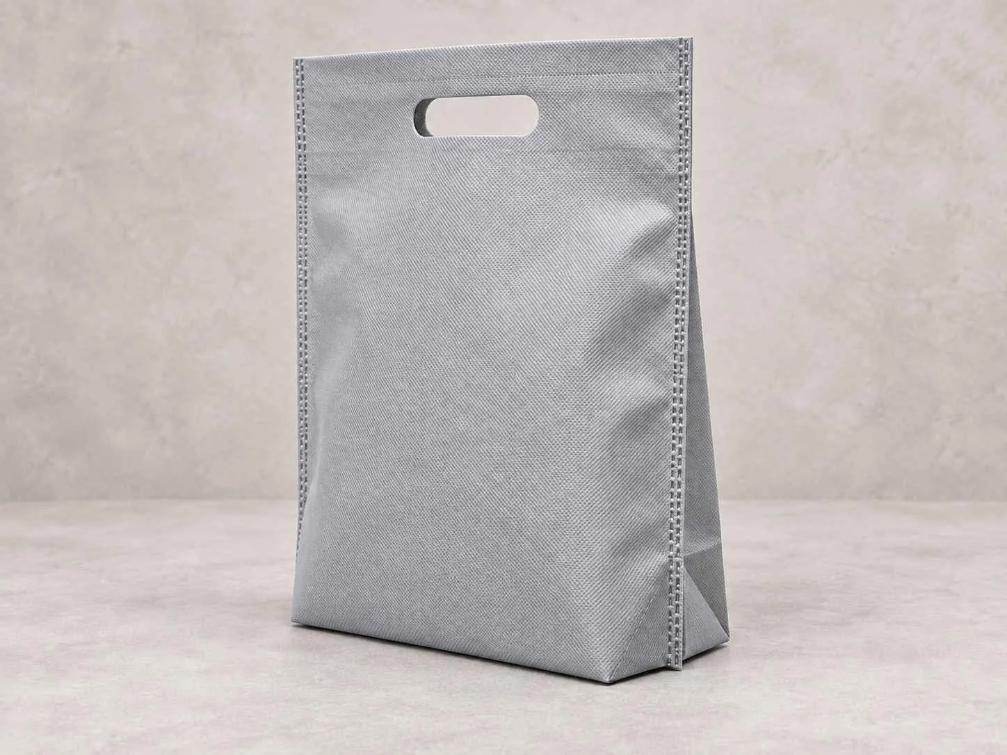 Silver metallic shopping bag with a handle troquelada at the top, standing upright on a light-colored surface with a plain neutral background.