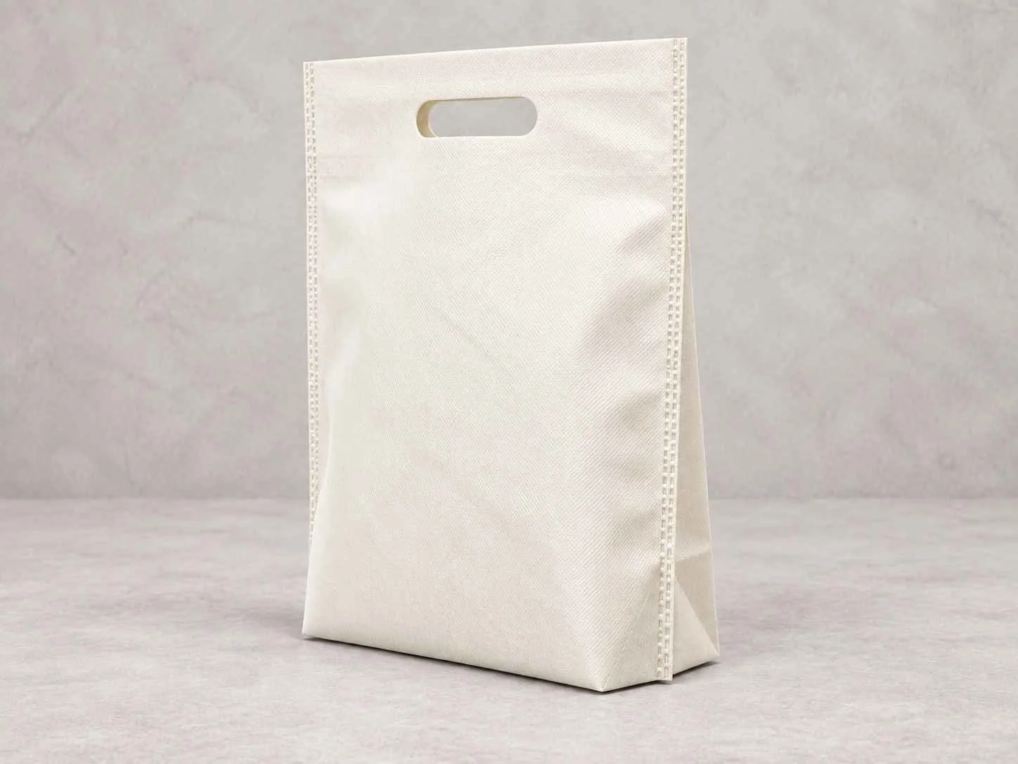 	
Una bolsa reutilizable color hueso plana con fuelle abajo de pie vertical sobre una superficie neutra contra un fondo neutro.
