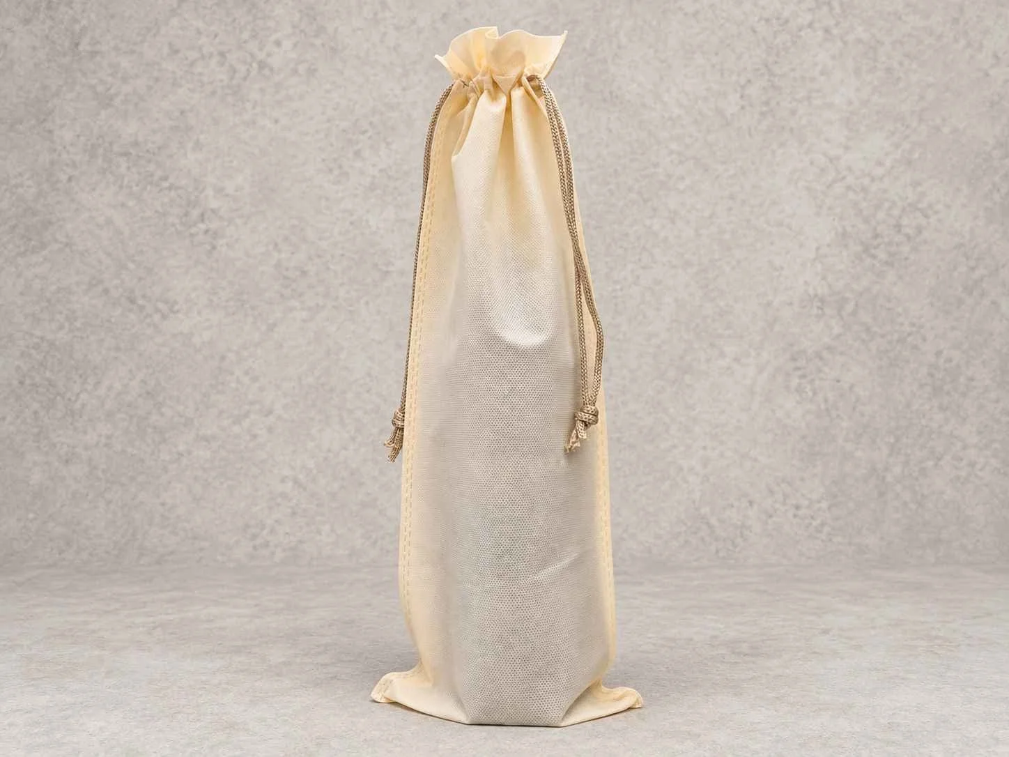 A beige cloth drawstring bag standing upright on a gray surface against a gray background.