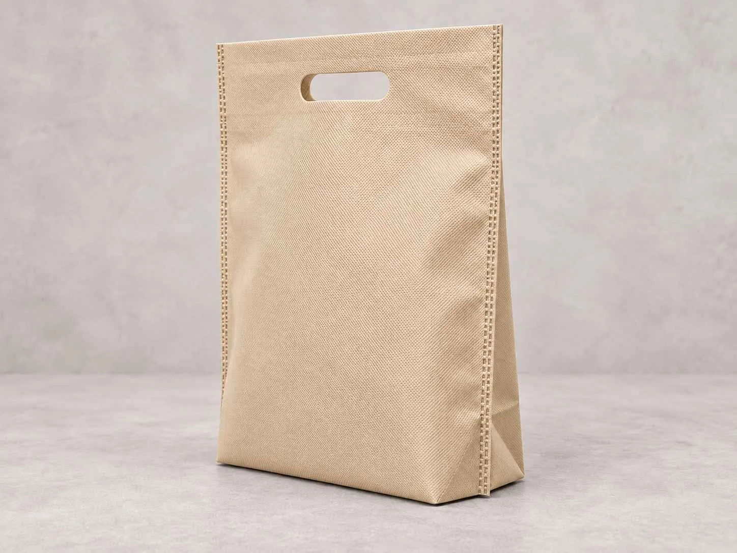 	
Una bolsa reutilizable beige de cambrel plana troquel con fuelle abajo de pie vertical sobre una superficie neutra contra un fondo neutro.
