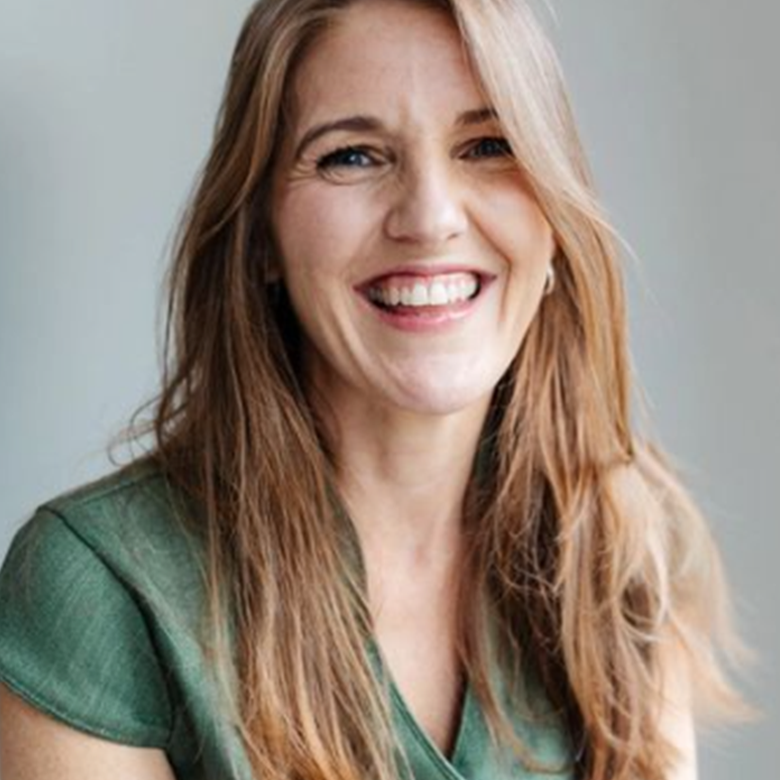Portrait of a smiling woman with long red hair, wearing a green top, against a plain background.
