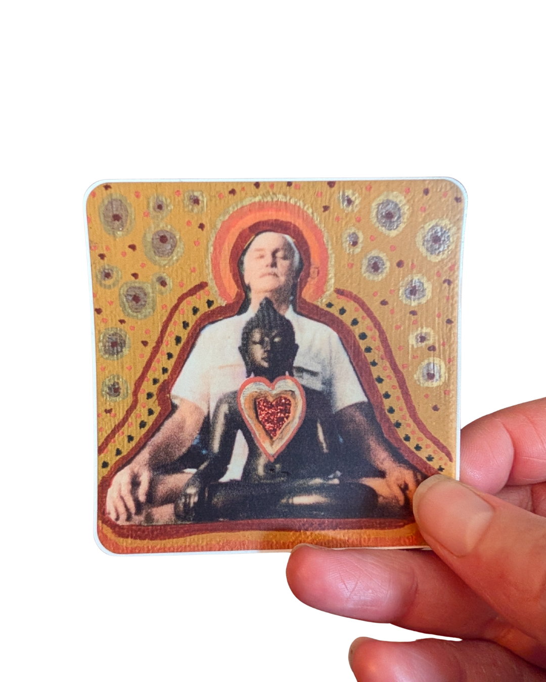 A hand holding a square card featuring an art piece with a woman praying, overlapping with a Buddha figure and a heart at the center, with a yellow, dotted, and swirled background.