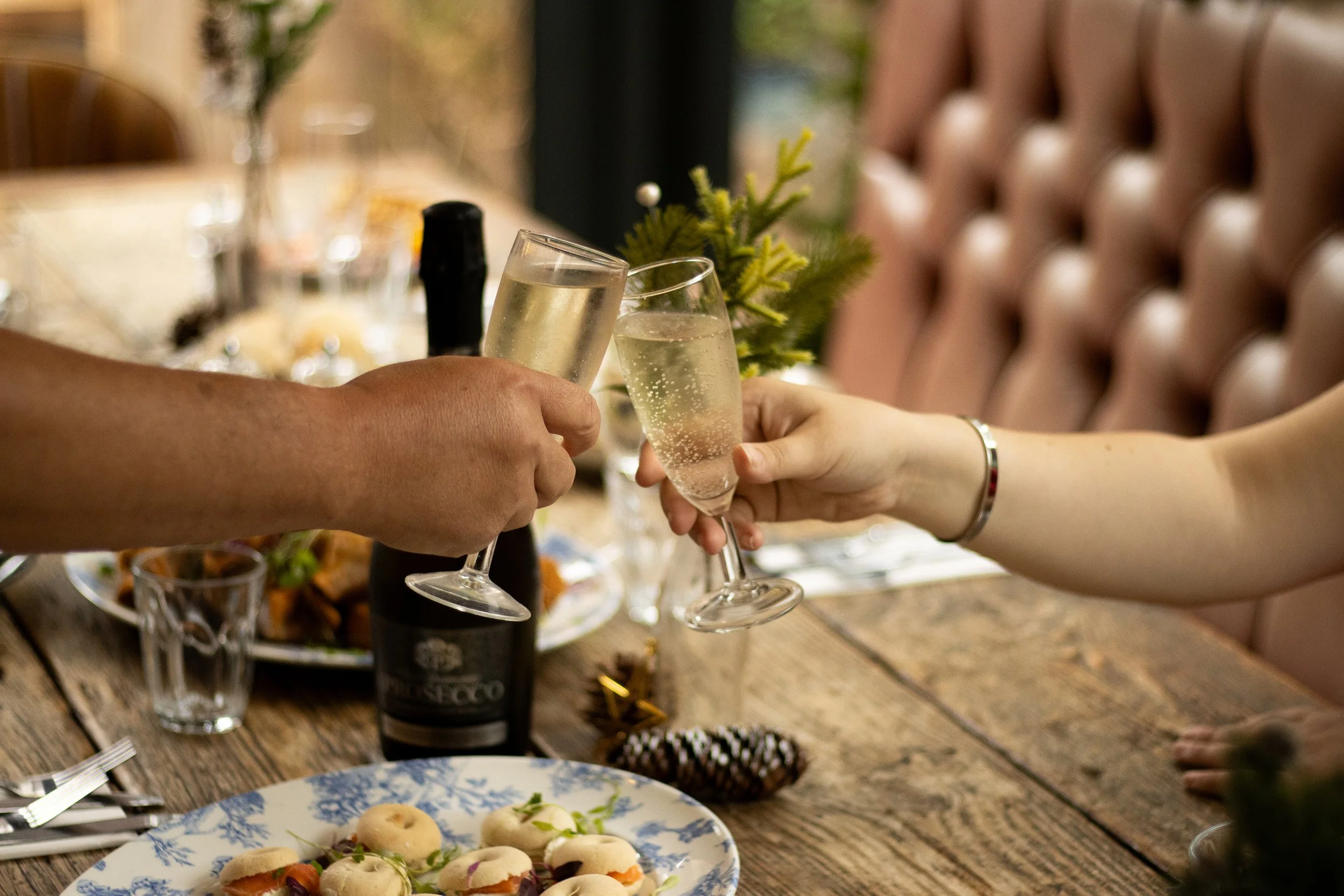 People clinking champagne glasses over a table set with assorted food and drinks at a celebration or gathering.