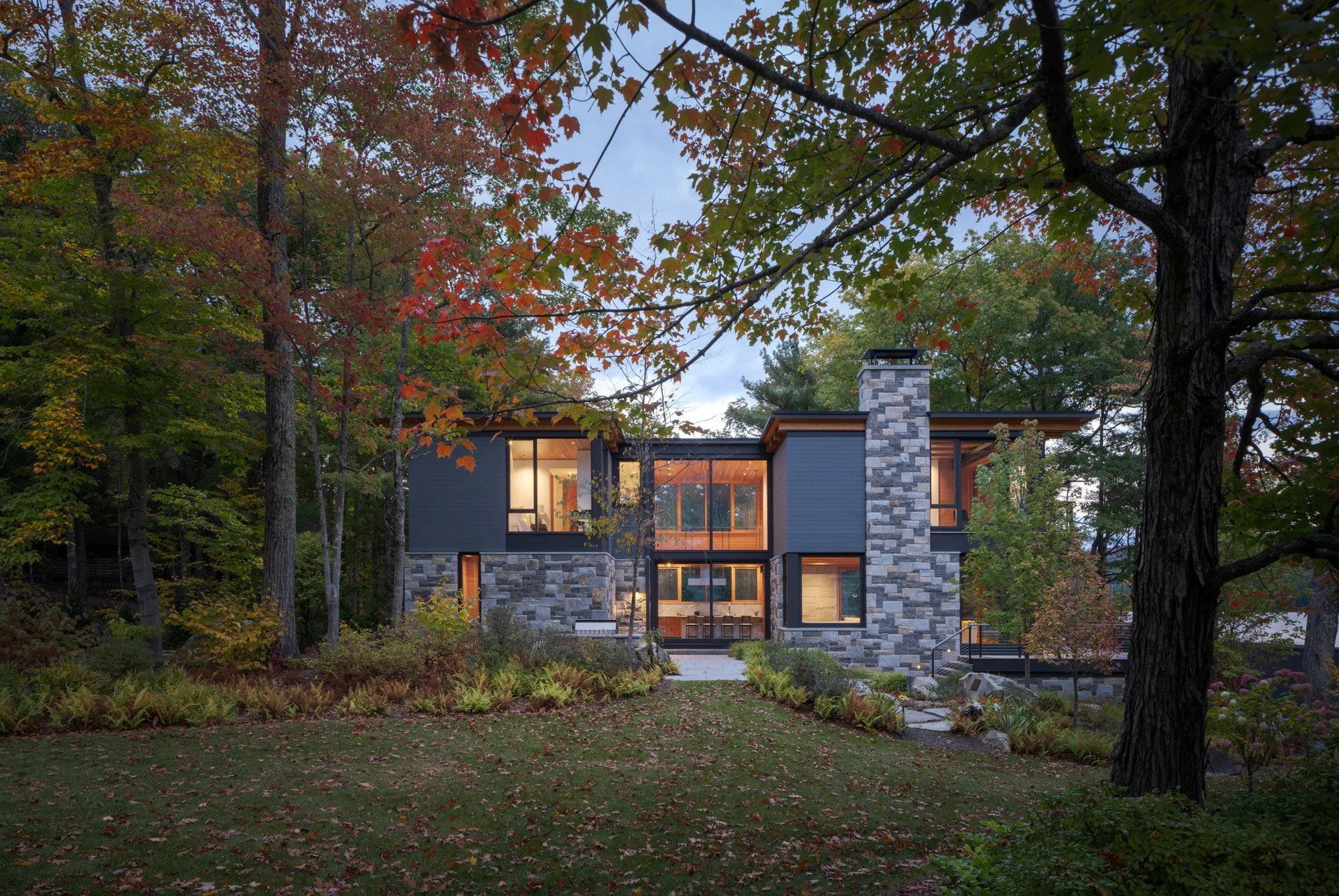 Cove House from the perspective of an existing guest house on the property. Plantings part to reveal an inviting stone patio. Large sliding glass doors open to the bright and airy kitchen, welcoming guests inside. 

Builder: @burpeehillconstruction
L