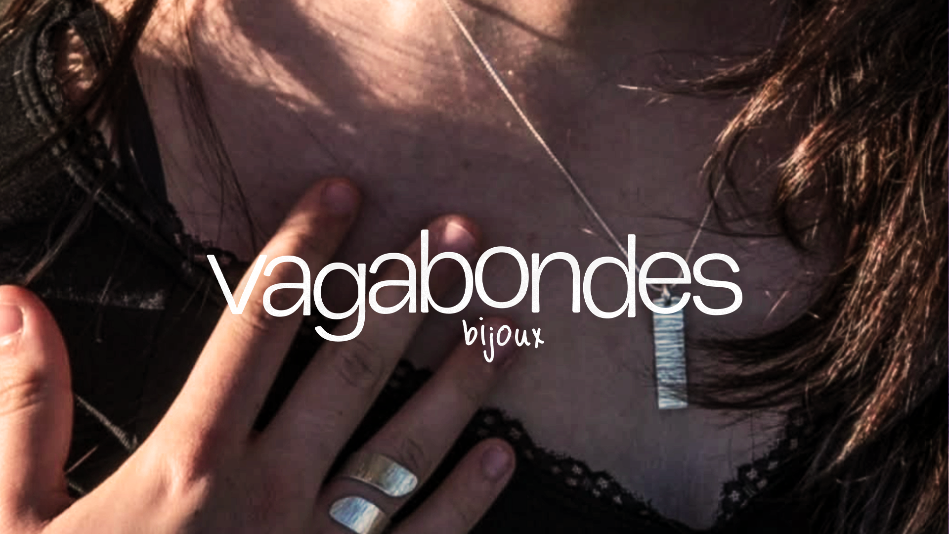 Une main portant une montre argentée touche le haut de la poitrine d'une femme portant un collier en diamant, avec le texte "vagabondes bijoux" superposé sur l'image.