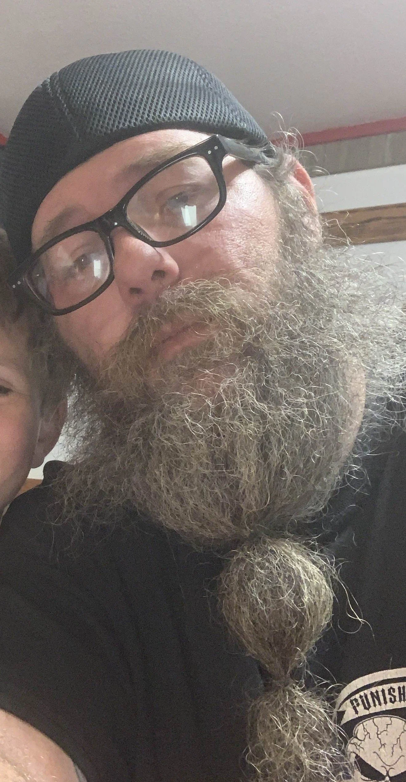 A man with glasses, a gray beard and wearing a black cap, posing indoors.