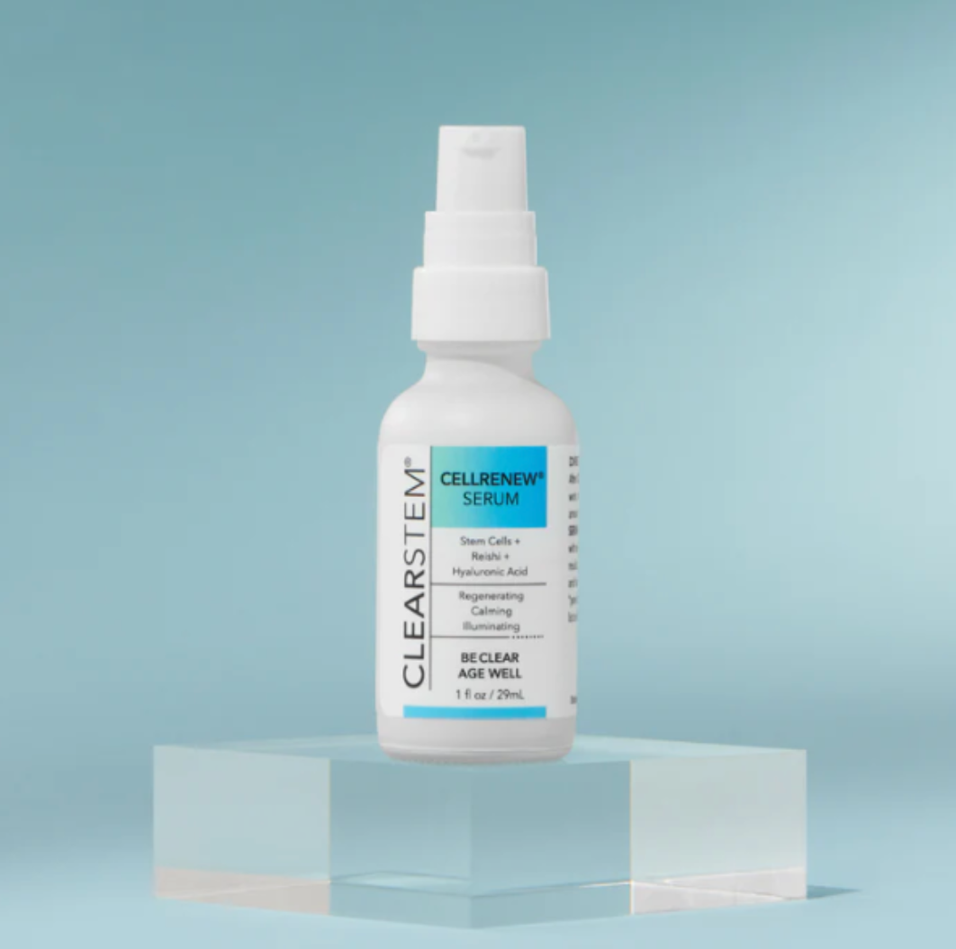 A small white spray bottle labeled CELLRENEW SERUM with a blue and black label, placed on a clear acrylic block against a light blue background.