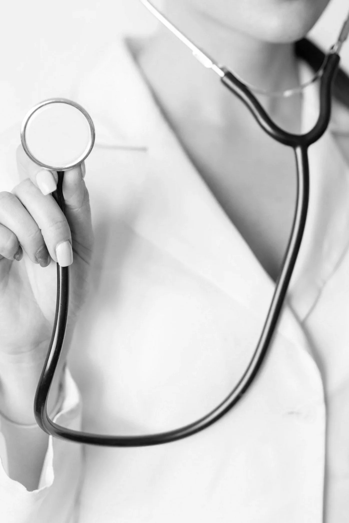 Close-up of a healthcare professional holding a stethoscope, with part of their white coat visible.