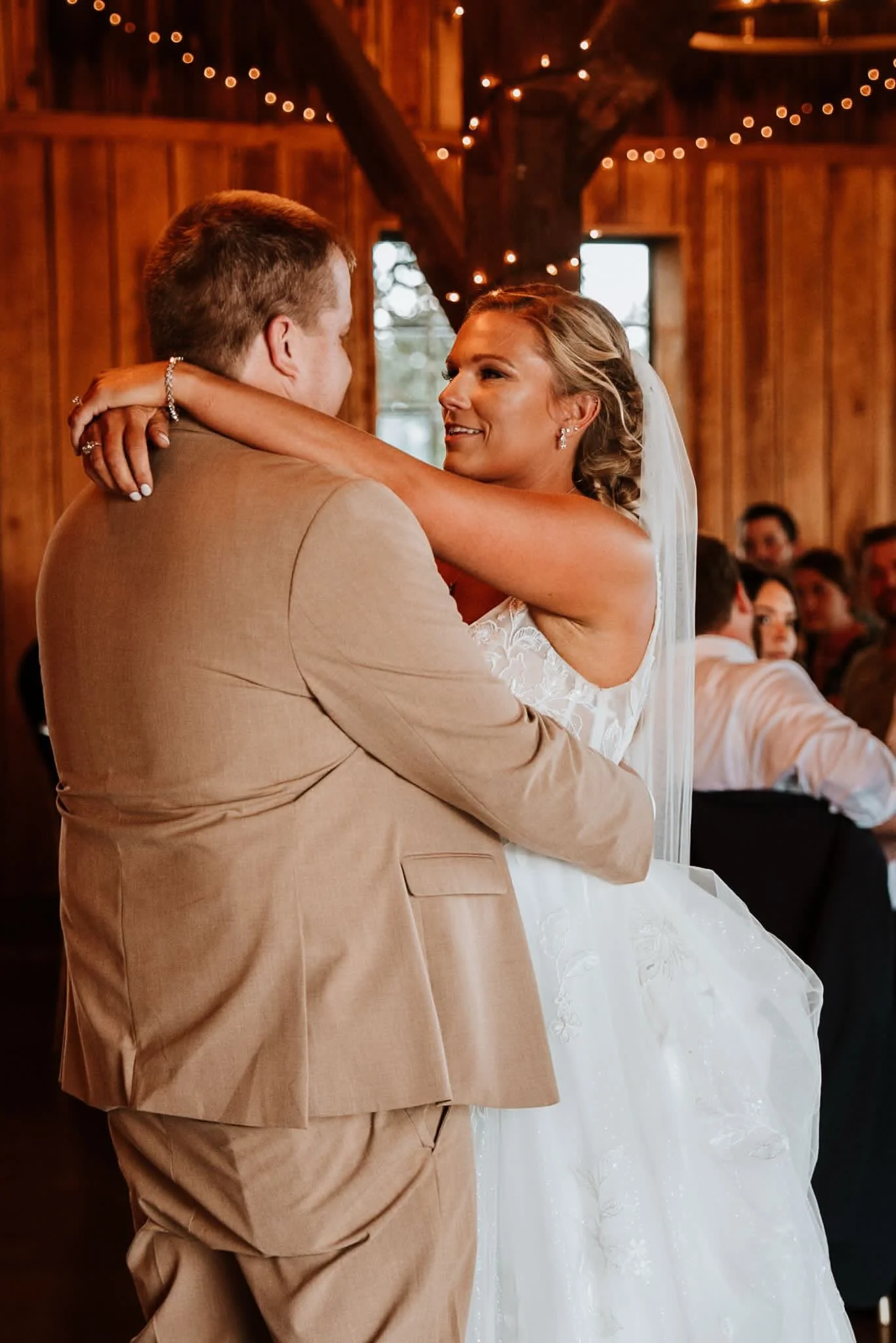 A bride and groom sharing a dance during their wedding in a rustic wooden venue with string lights.