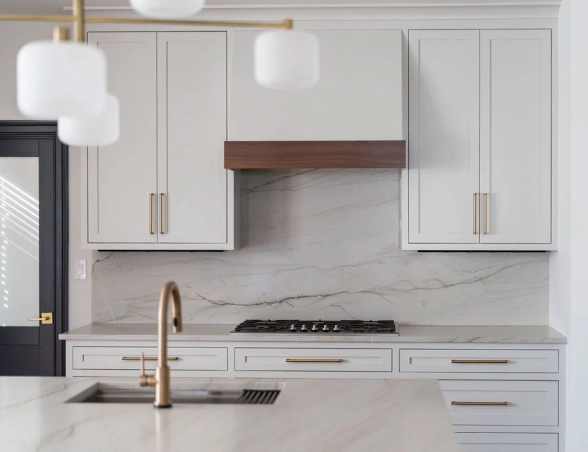 Custom white kitchen cabinetry with stone backsplash, brass hardware, and wood range hood detail by Rift & Quarter