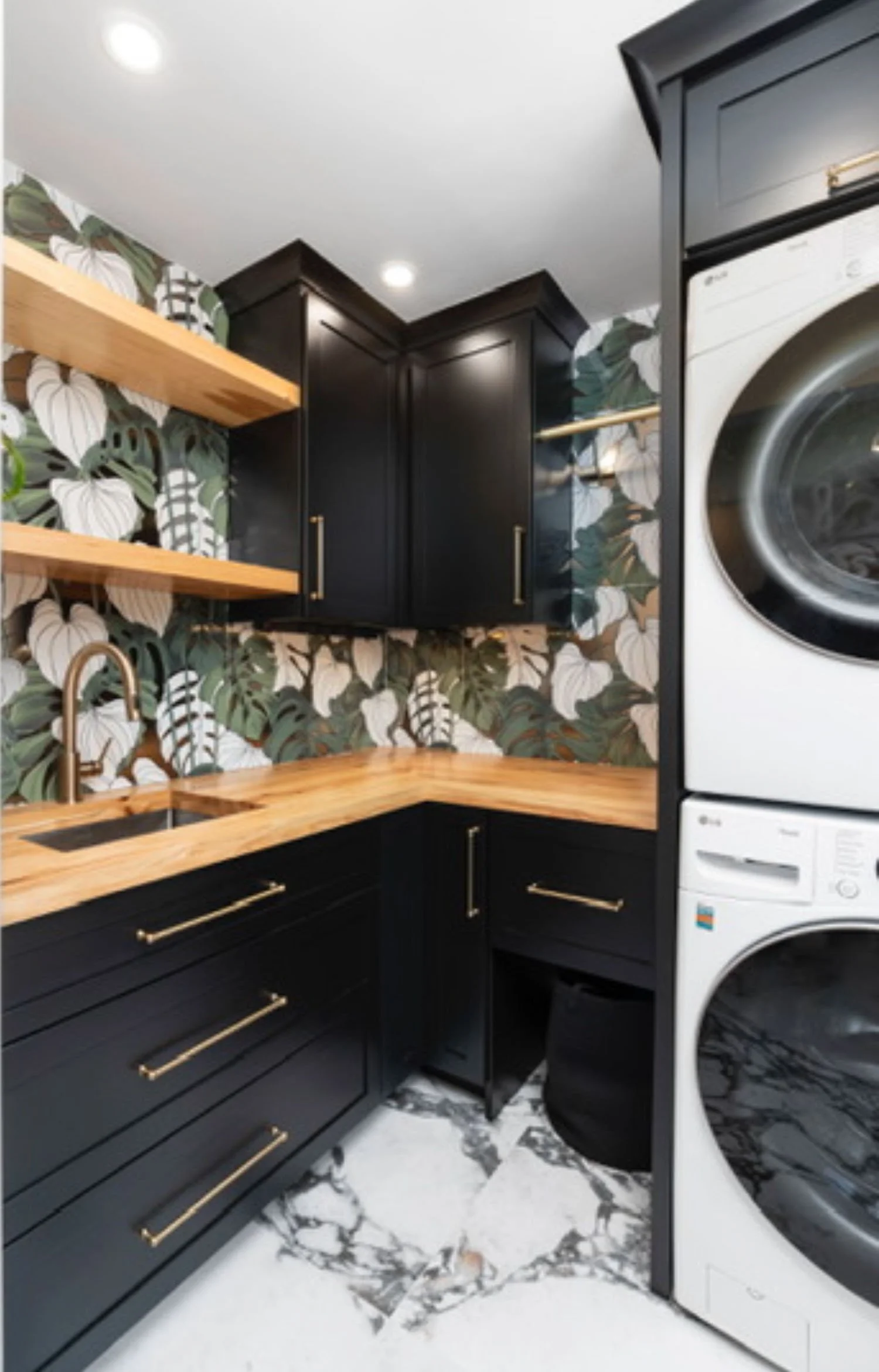 Custom laundry room cabinetry with dark cabinets, wood shelving, patterned wallpaper created by Rift & Quarter