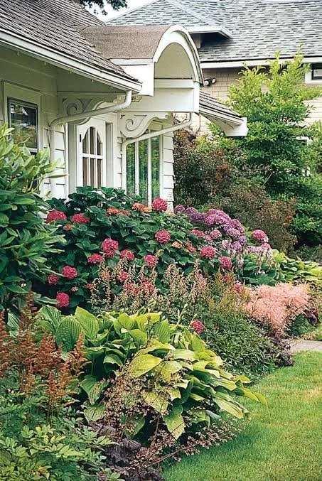 A house with a garden full of pink and purple flowers and lush green shrubs and trees.