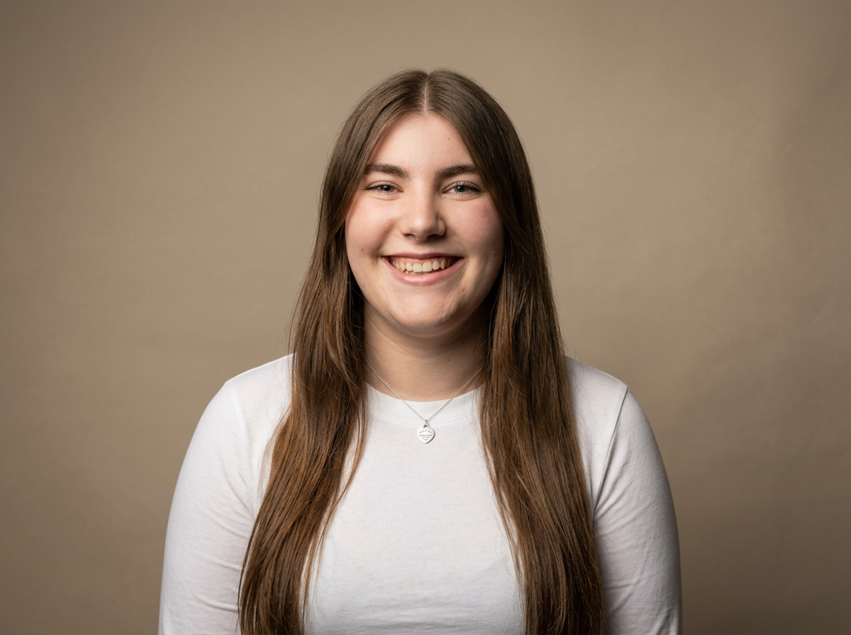 A young woman with long brown hair, smiling and wearing a white shirt, standing against a neutral background.