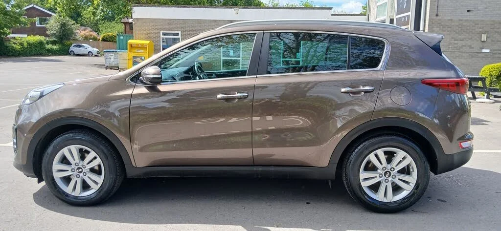 Side view of a brown Kia Sportage SUV parked outside a building.