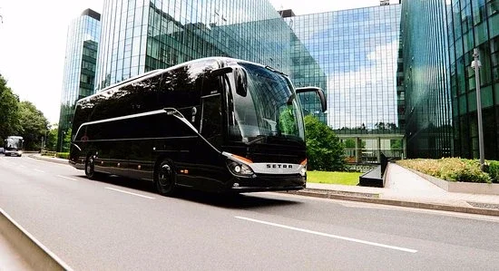 Black Setra coach bus parked outside a modern glass office building