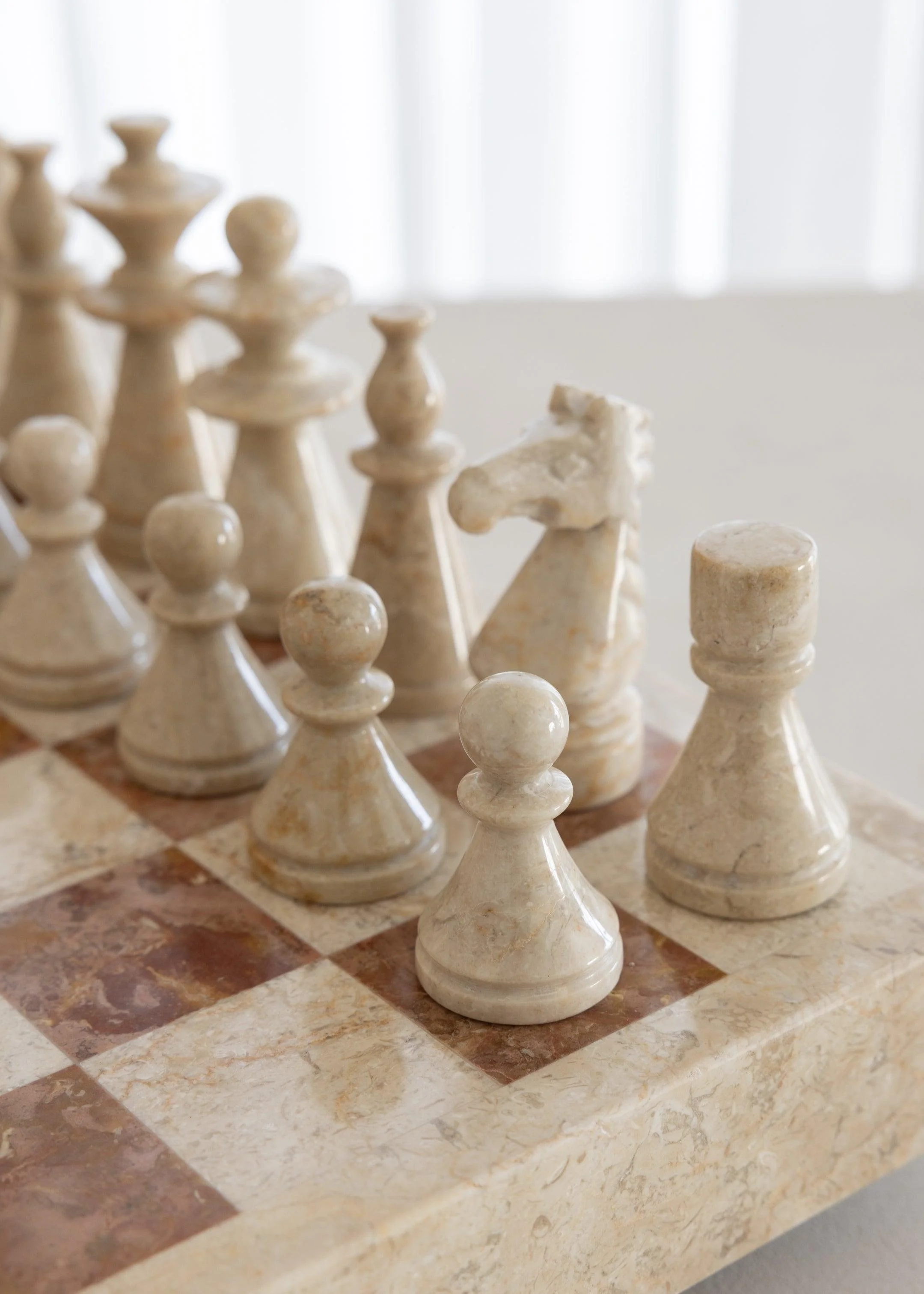 Jeu d'échecs en marbre blanc, pièces sur un plateau en marbre à carreaux de différentes couleurs.