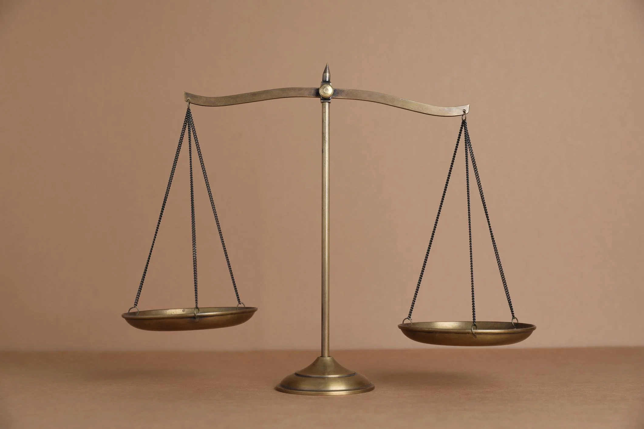 Une balance ancienne en pièces de métal avec deux plateaux suspendus, placée sur une surface plane, contre un fond beige.