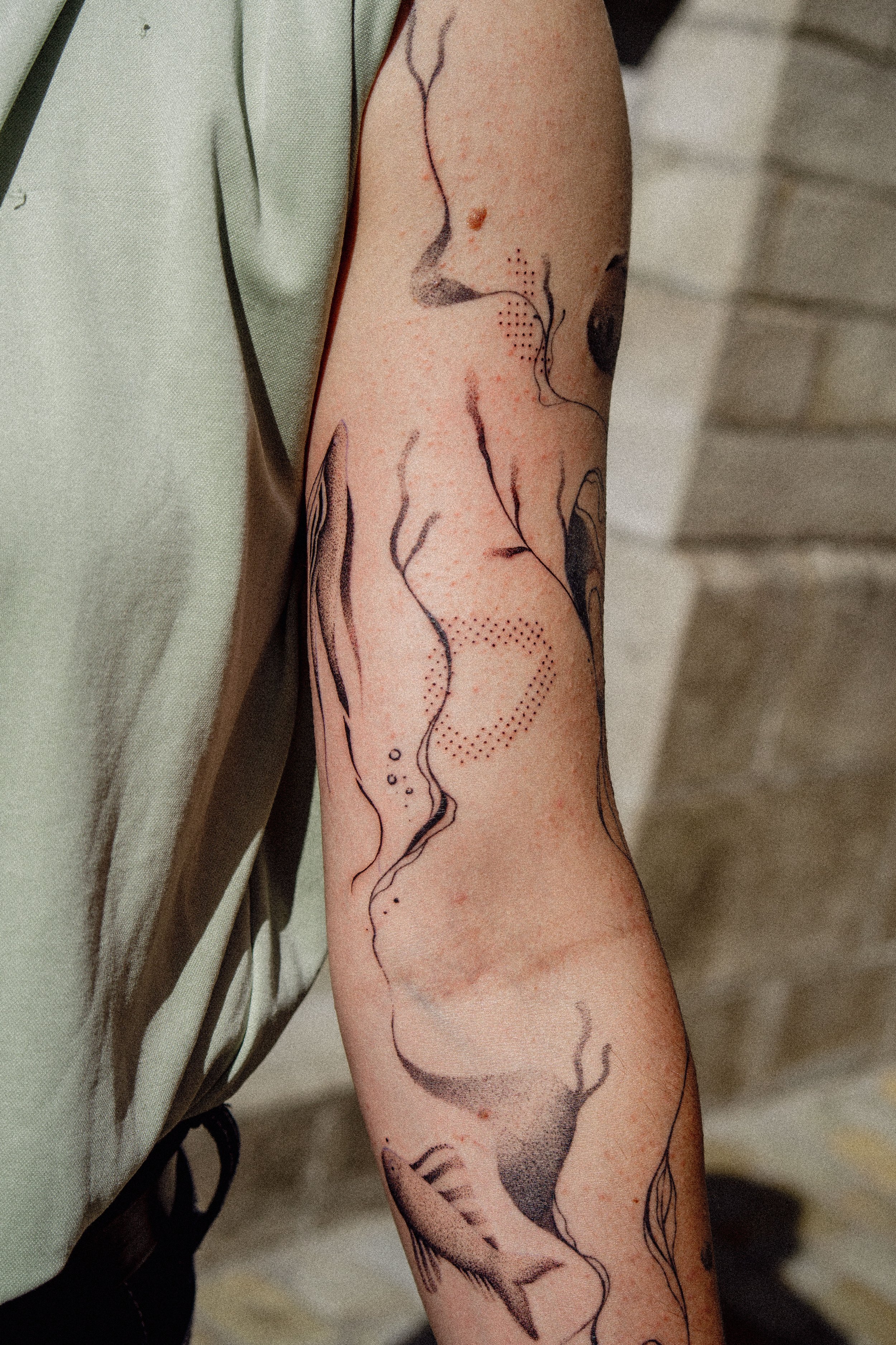 Tatouage abstrait et délicat sur le bras d'une personne, représentant des lignes sinueuses et des formes fluides en noir et gris.