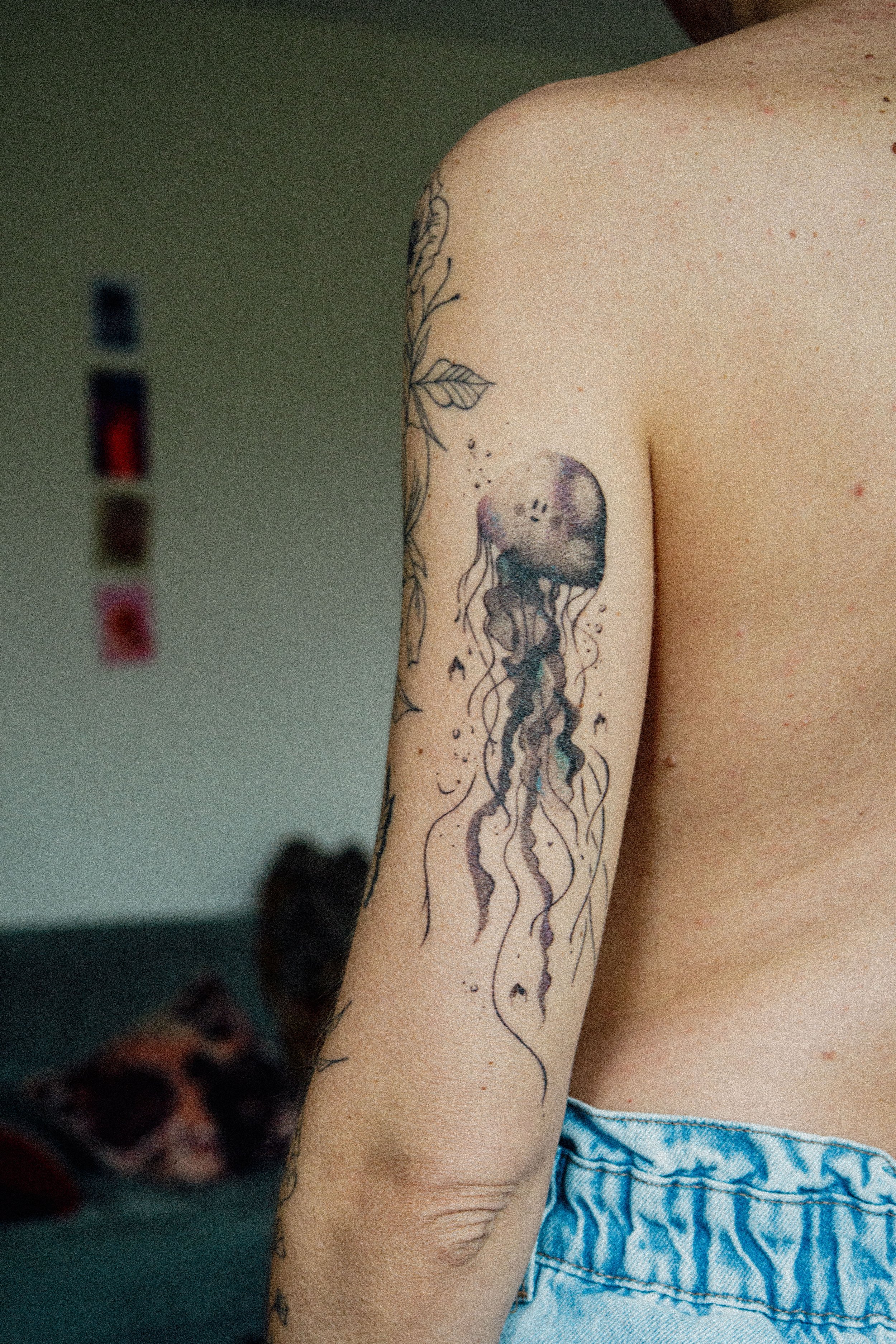 Tatouage d'une méduse sur le bras d'une personne, portant un débardeur et un jean.