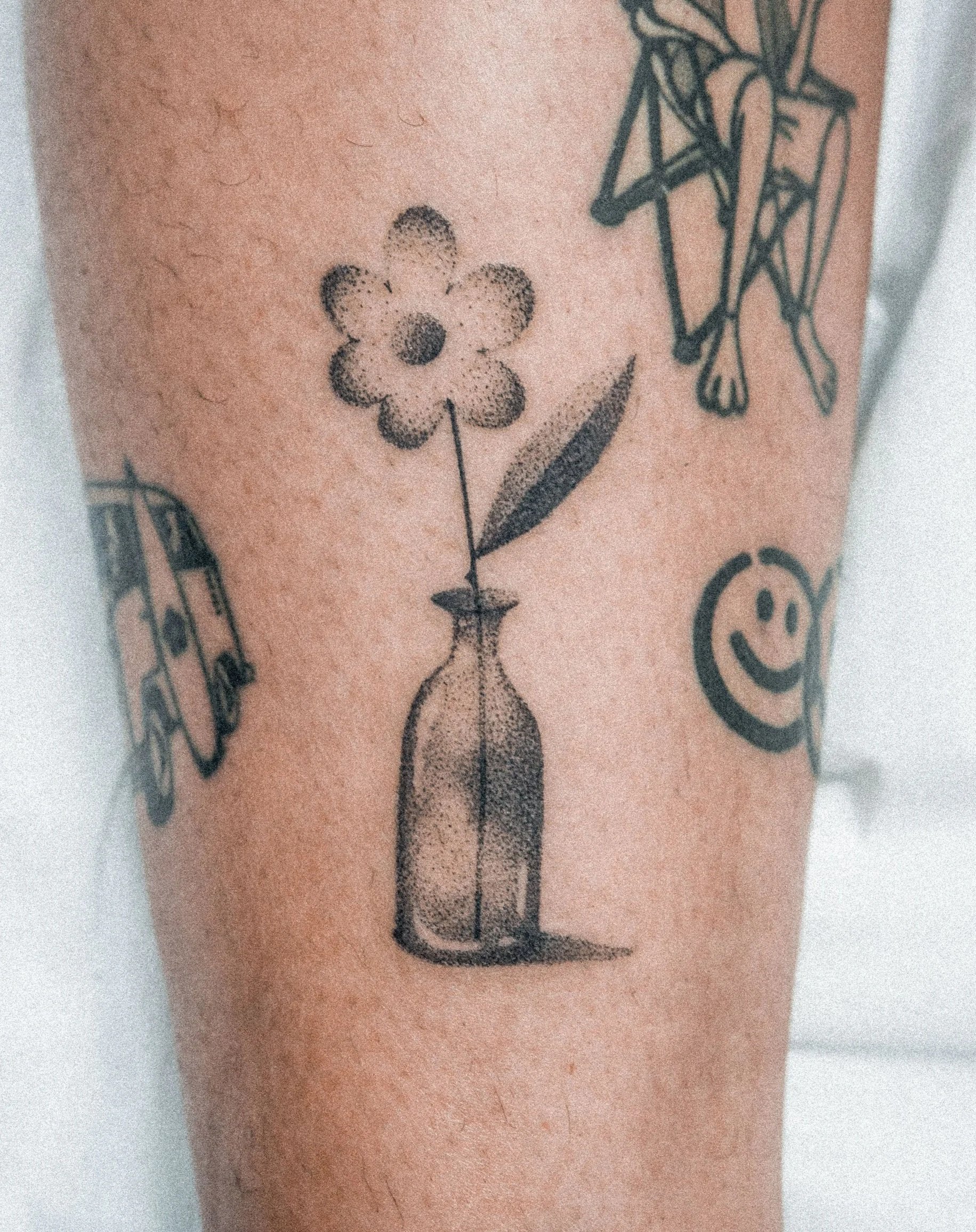 Tatouage en pointillé d'une bouteille avec une fleur dans le haut, sur la peau