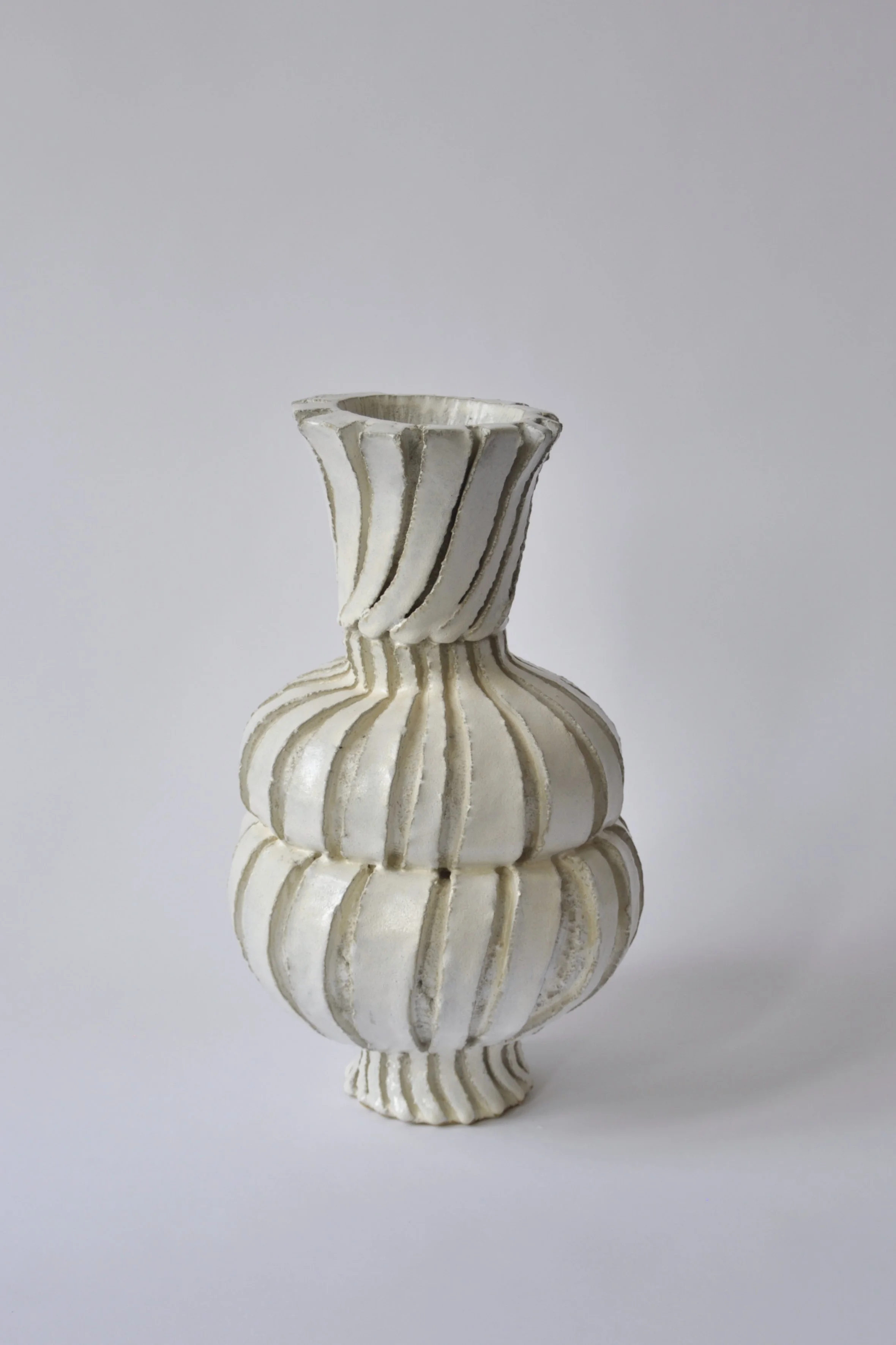 weiße Keramikvase mit vertikalen Linien auf einem weißen Hintergrund, das Bild ist hochkant und fokusiert auf die Vase