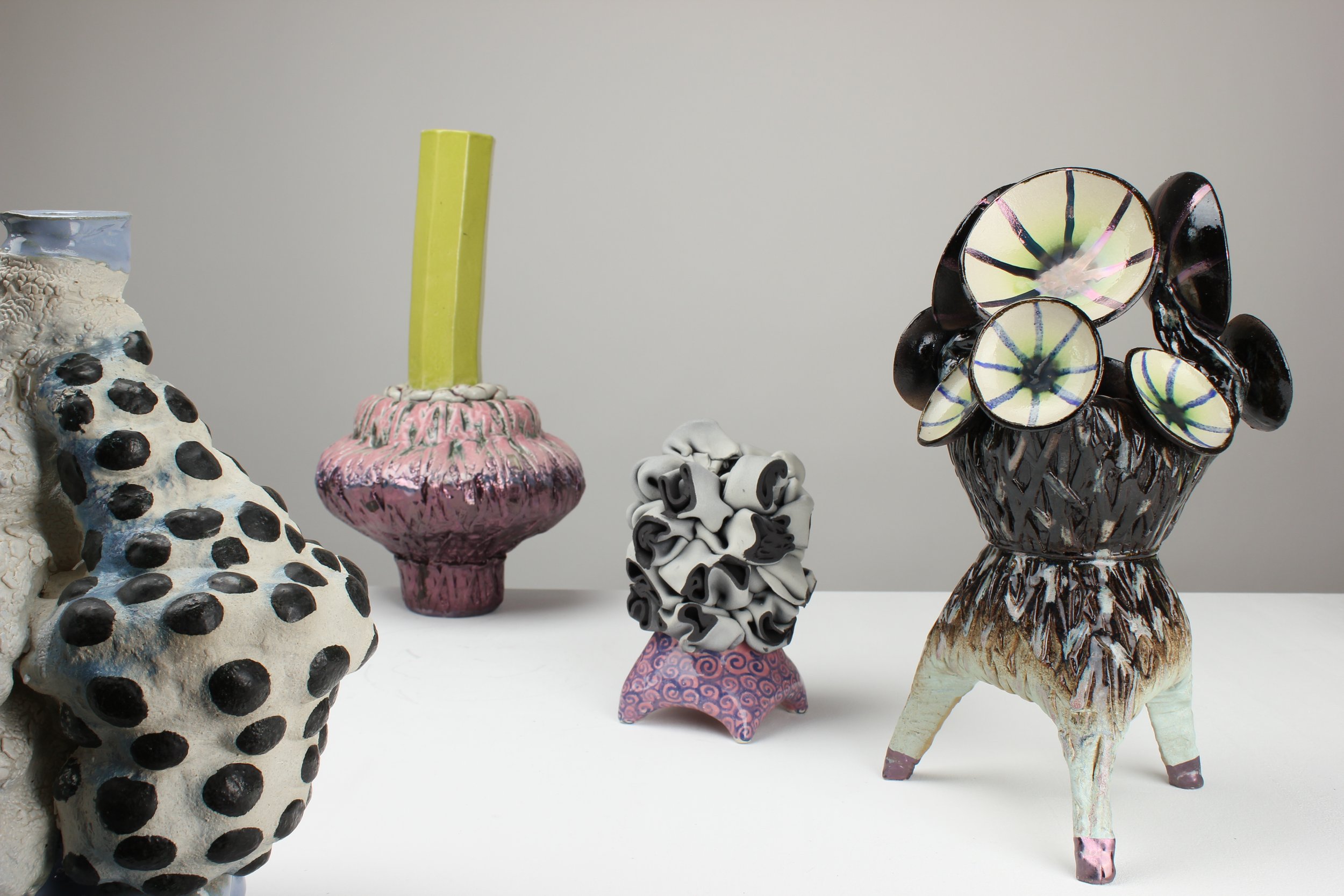 Verschiedene kunstvolle Keramikskulpturen, darunter eine Skulptur eines Tieres, eine Vase mit einer großartigen Struktur, eine Keramikskulptur mit schwarzen und weißen Mustern und eine Vase mit bunten, kreisförmigen Glasdekorationen.