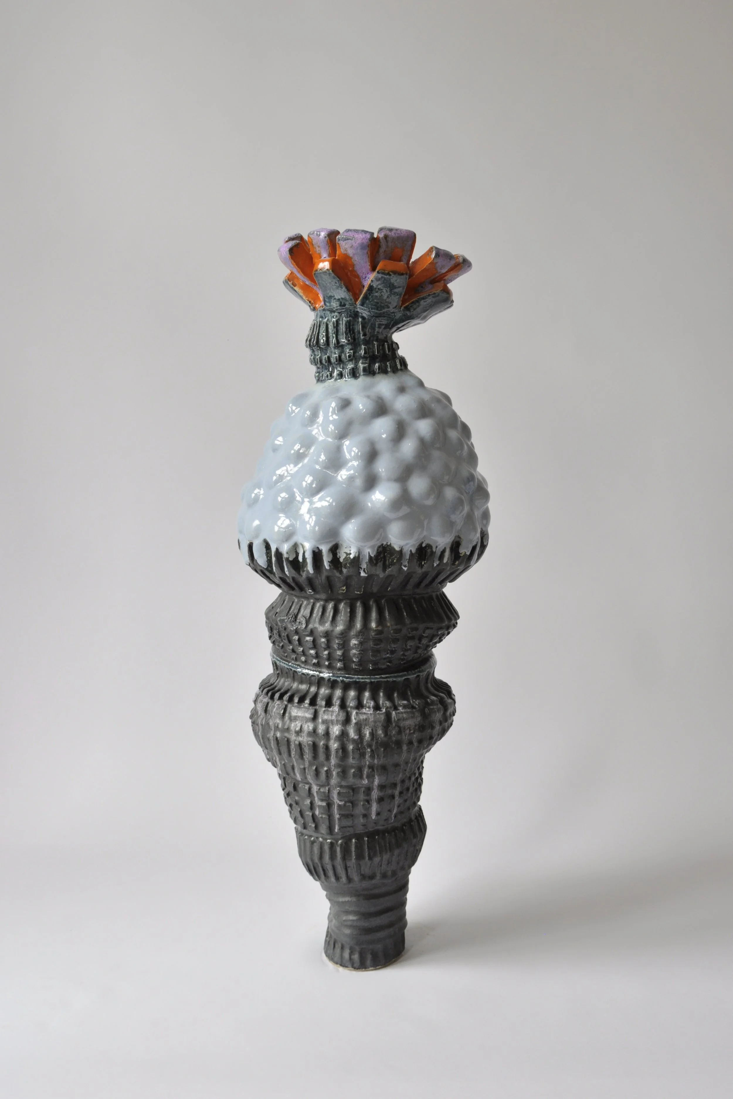 Skulptur eines schwarzen Waffeleis, das an einen Blumenstrauß erinnert, mit farbigen Details an der Oberseite, vor hellem, neutralem Hintergrund.