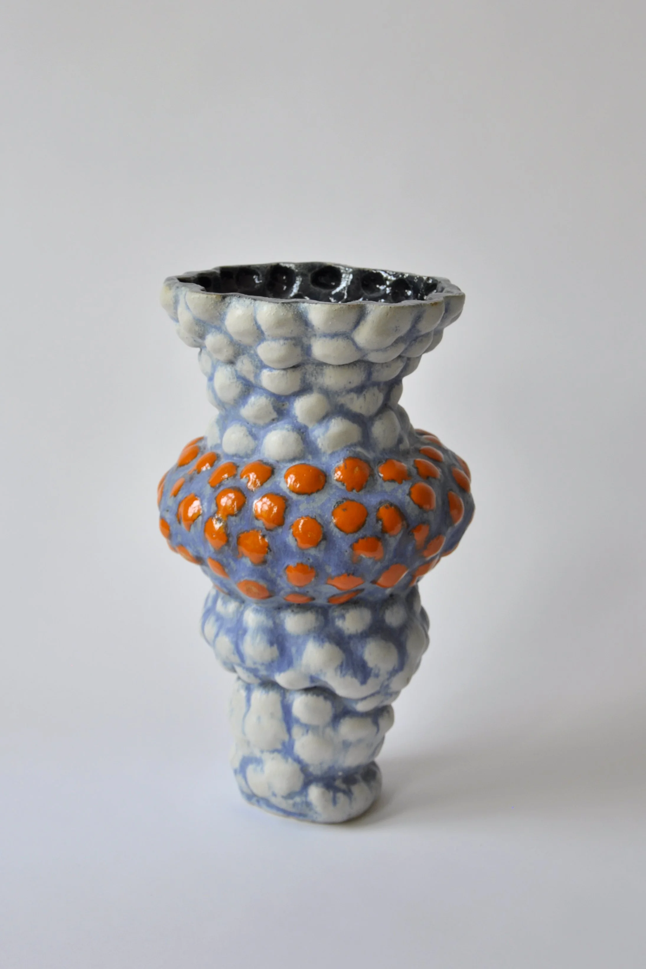 Keramikvase mit strukturierter Oberfläche in Blau, Weiß, Orange und Schwarz vor hellem Hintergrund
