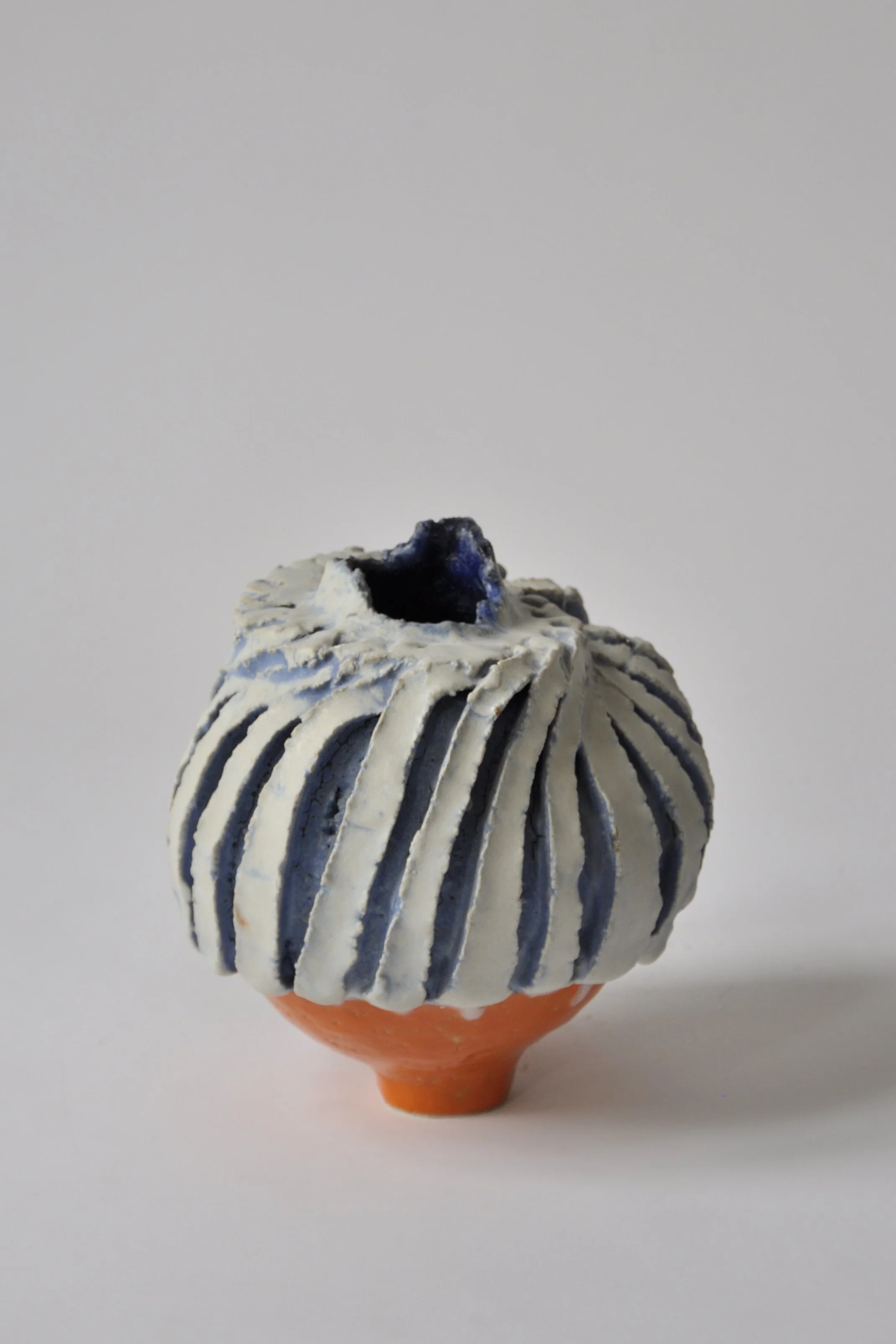 Keramikvasen mit blauer und weißer Verzierung, auf einem orangefarbenen Ständer, auf weißem Hintergrund.