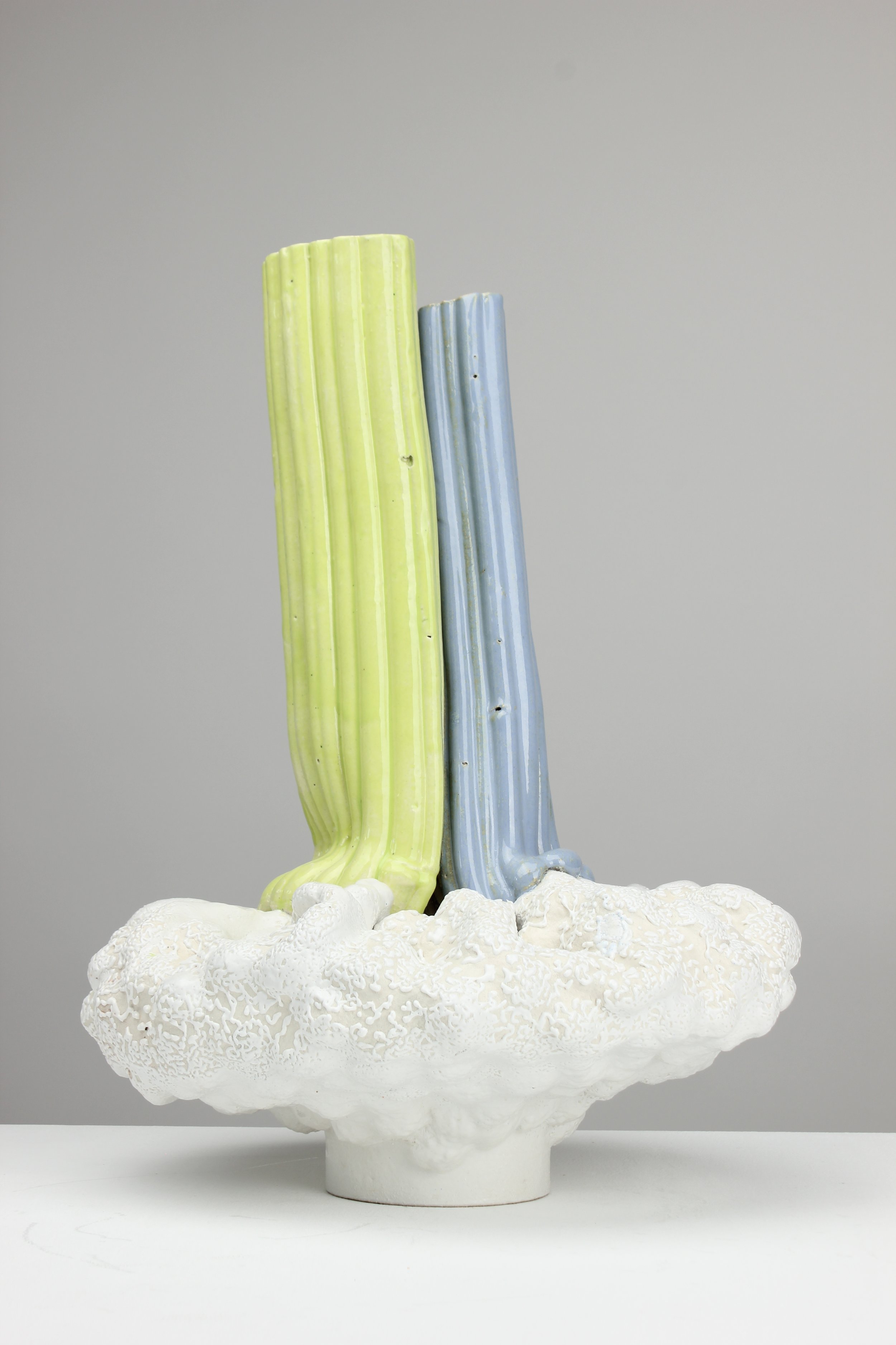 Kunstinstallation mit drei bunten, vertikal angebrachten, plastischen Elementen in verschiedenen Farben (Gelb, Blau, Lila), auf einer weißen, originellen, strukturieren Basis, die an einen Pilz erinnert.